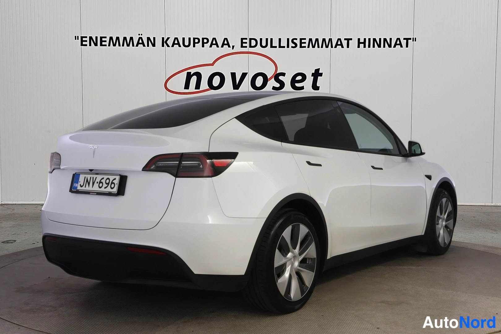 Takaviisto: Valkoinen Tesla Model Y takakulmakuvassa nokka oikealle, rekisterikilpi, studio-tausta.