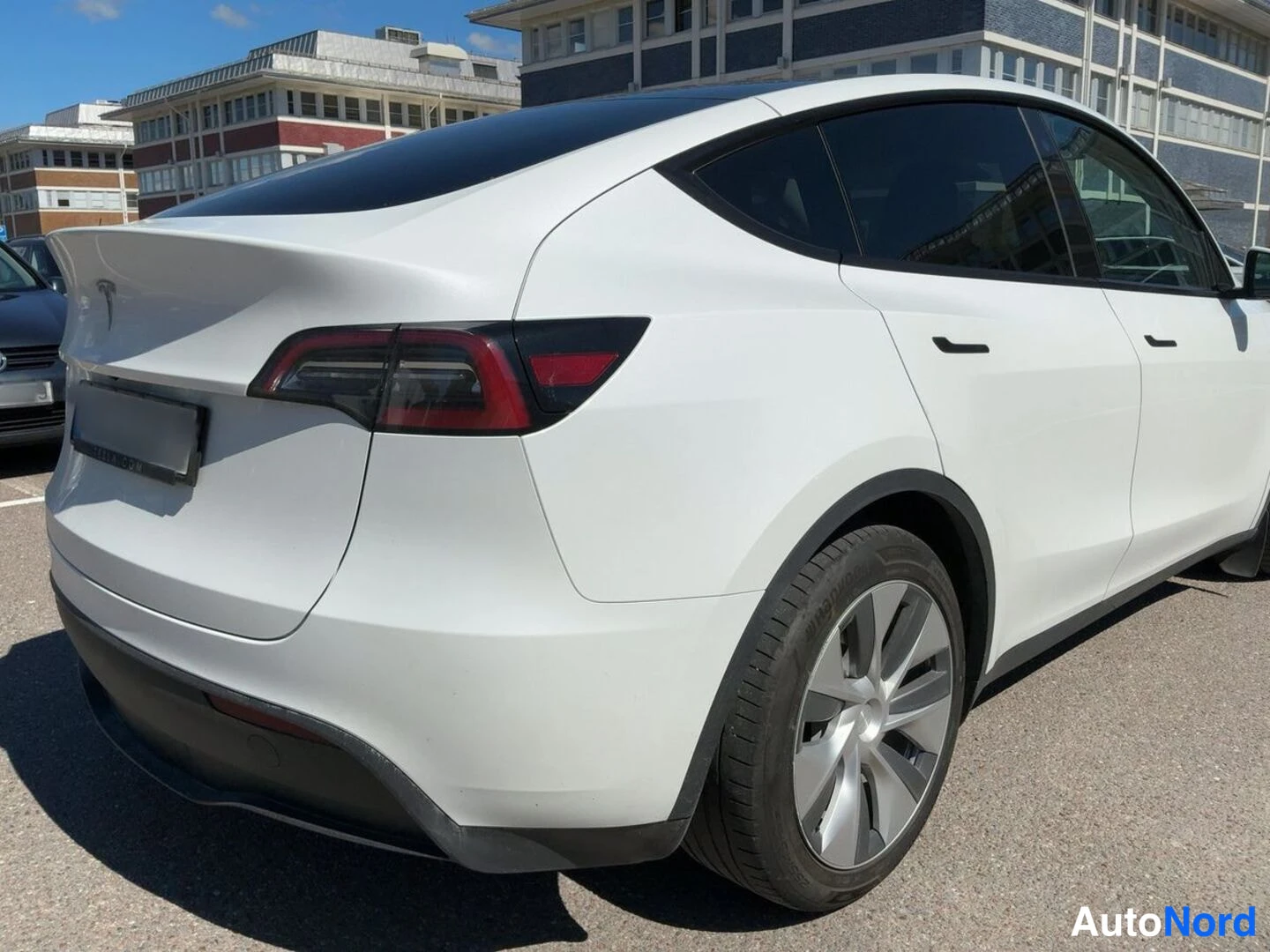 Takaviisto: Kuvassa näkyy valkoisen Tesla Model Y -auton takalauta ja oikea sivu. Takavalaistimet, rekisterikilven pelti ja takapuskuri ovat selkeästi näkyvissä.