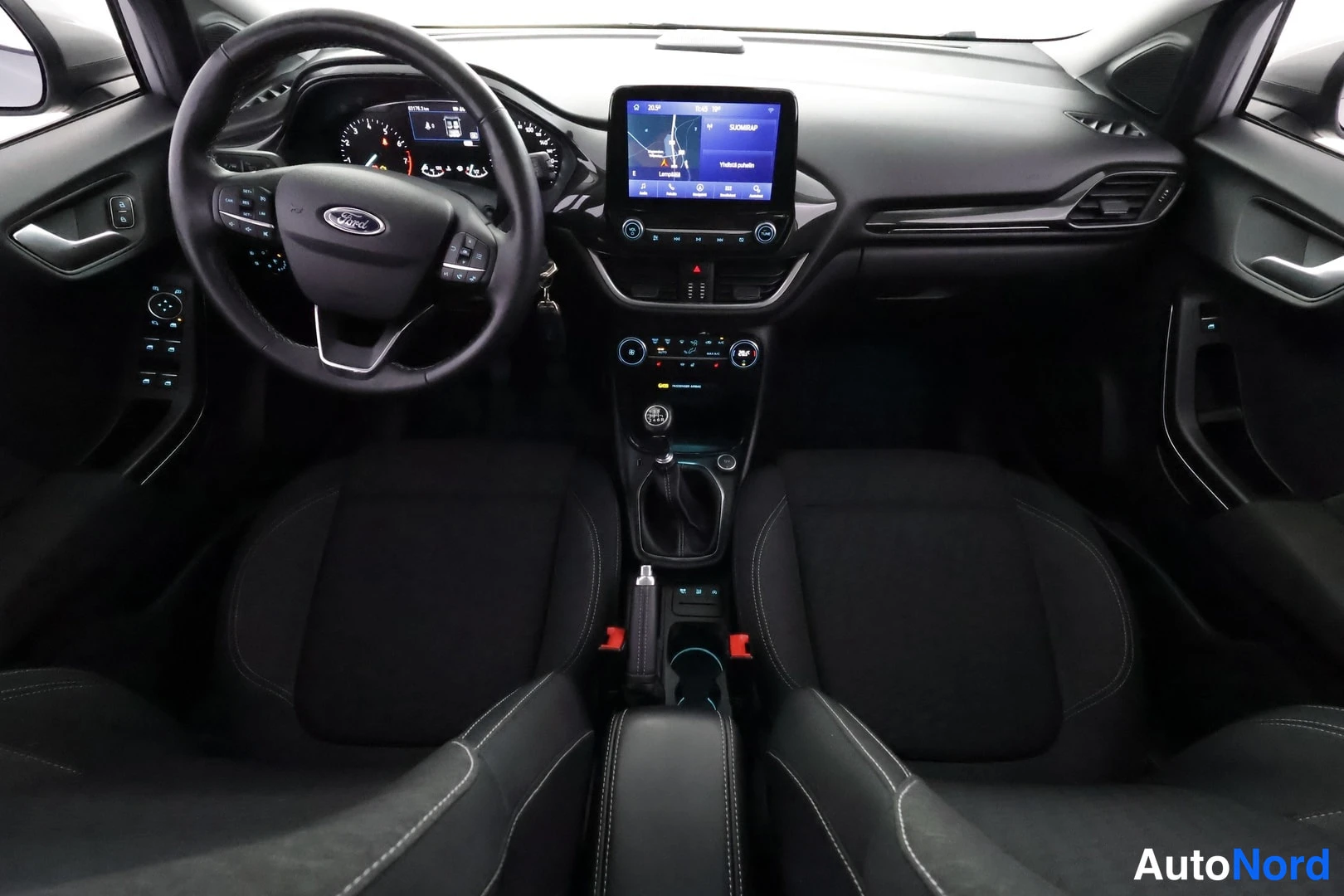 Ohjaamo: Front cabin interior view of a black dashboard and front seats. A touchscreen display for navigation is active in the center console above climate controls. A m