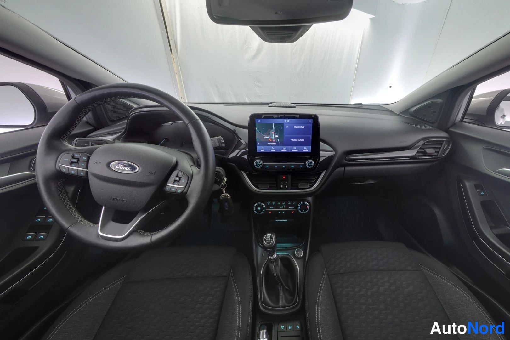Edestä: Ford Puman ohjaamo: Ford-merkkinen ohjauspyörä, keskellä kosketusnäyttö navigaatiossa, manuaalivaihdevipu ja kaksi etuistuinta.