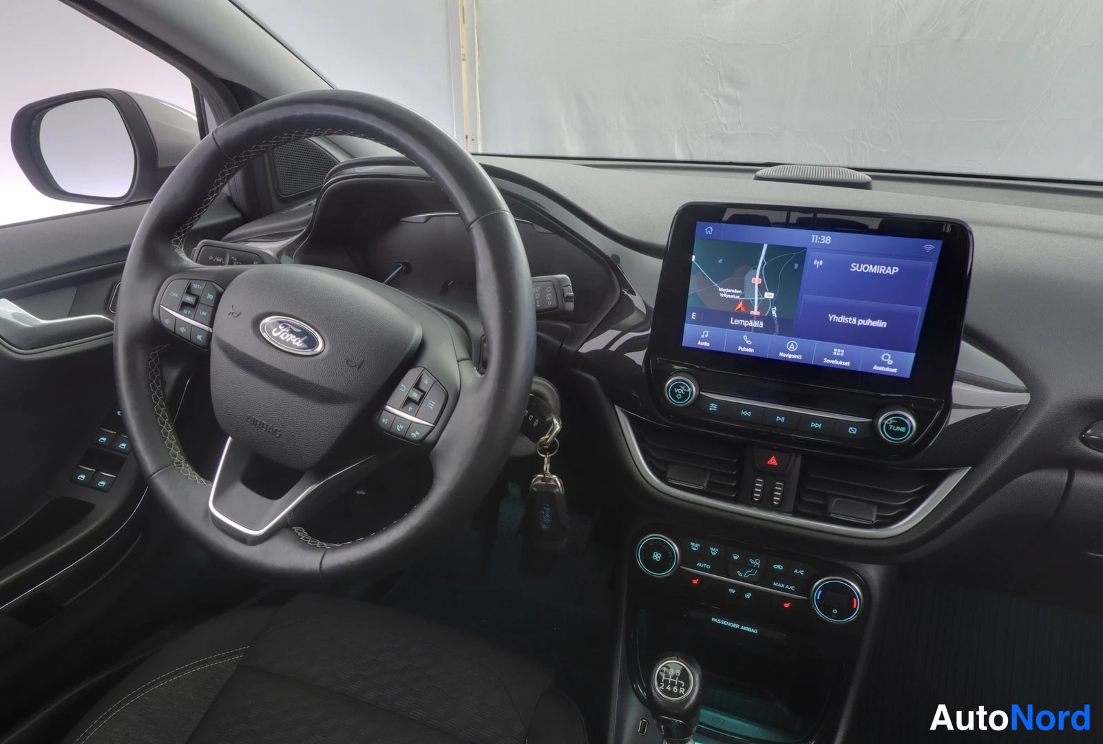 Edestä: Ohjauspyörä Ford-merkillä, kosketusnäytöllä navigaatio (Lempäälä) ja teksti 'Yhdistä puhelin', alla ilmastointipaneeli ja manuaalivaihdevipu.