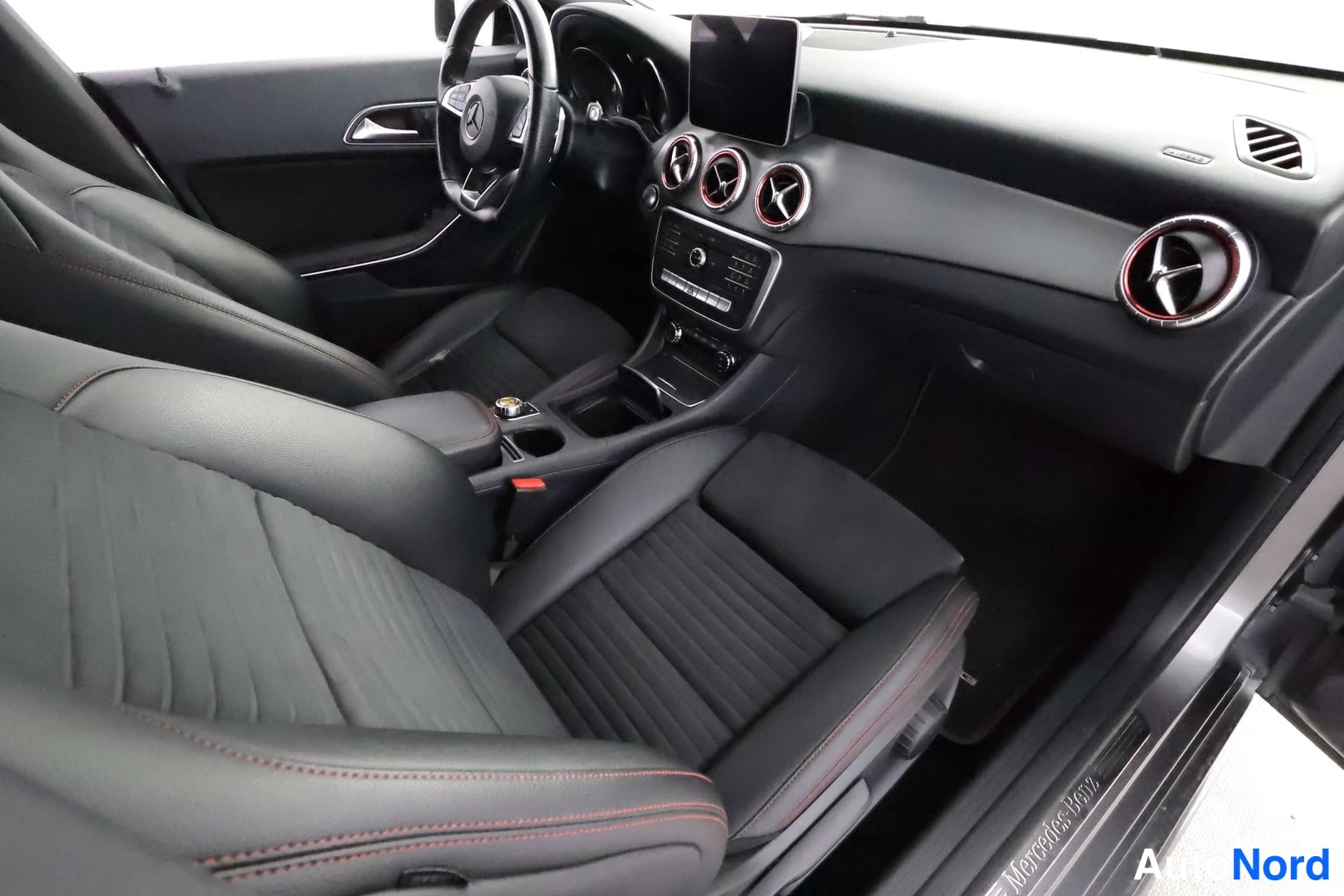 Yksityiskohta: Mercedes-Benz CLA:n sisätilat vasemmalta: mustat uritetut istuimet punaisilla ompeleilla, ohjauspyörä, keskikonsoli ja kokoonpanollinen näyttö kojelaudassa.