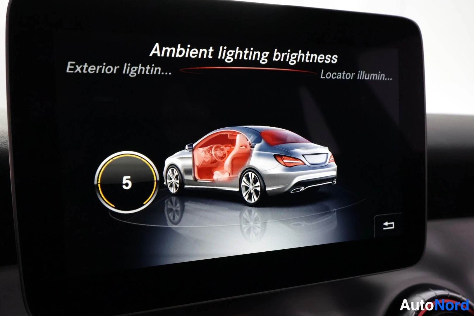 Yksityiskohta: Lähikuva auton infotainment-näytöstä, jossa valikko 'Ambient lighting brightness' ja ympyrävalitsin arvolla 5; sivuvalikot 'Exterior lightin...' ja 'Locator ill