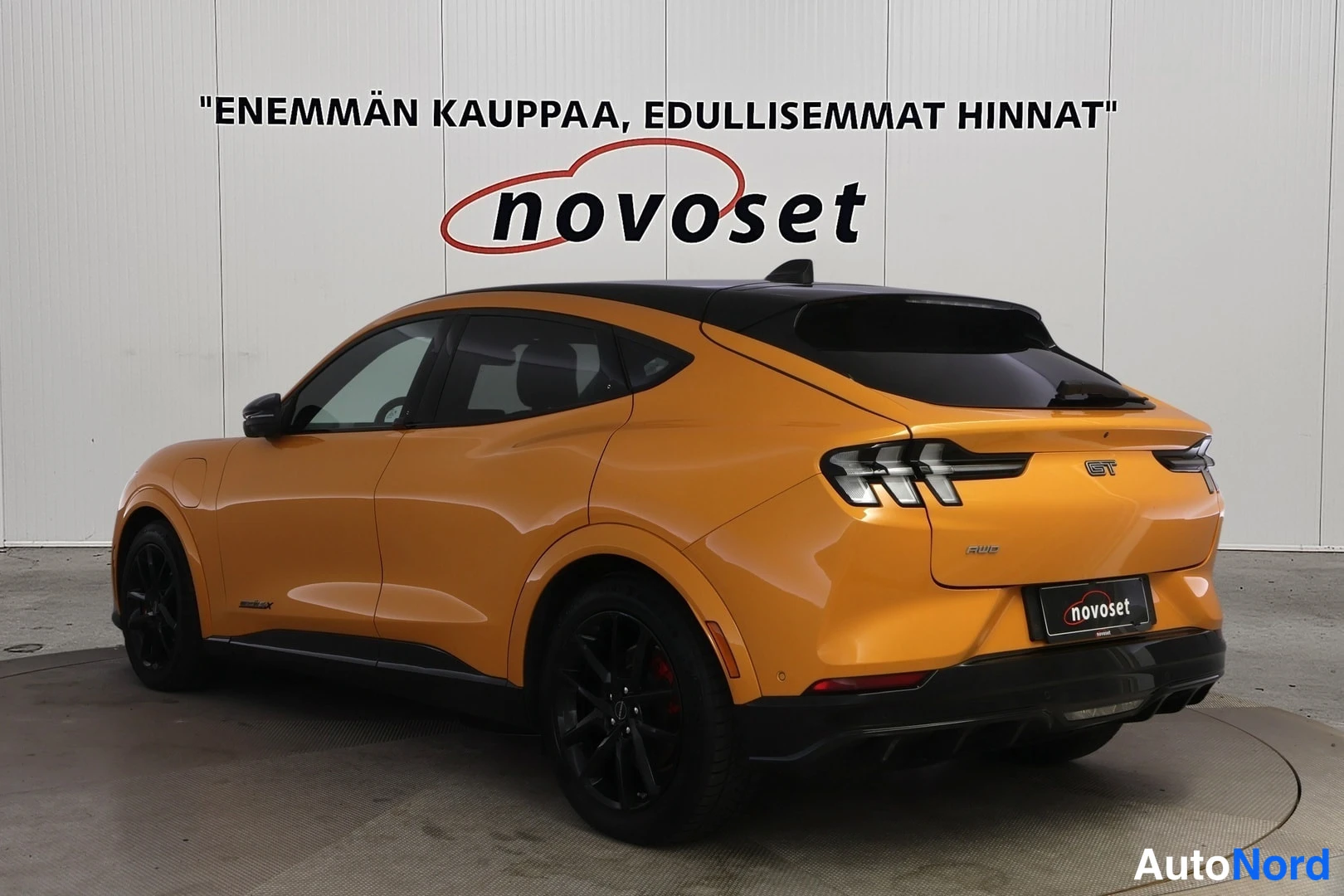 Takaviisto: Oranssi Ford Mustang Mach-E takaviistosta, perä kuvan oikeassa laidassa; musta katto ja mustat kevytmetallivanteet.