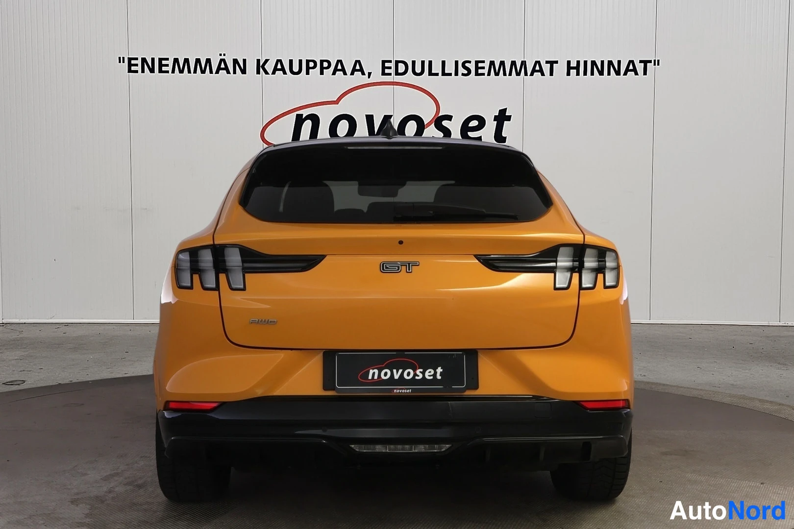 Takaa: Oranssi Ford Mustang Mach-E suoraan takaa kuvattuna; peräluukussa GT-merkintä ja musta alatunniste.