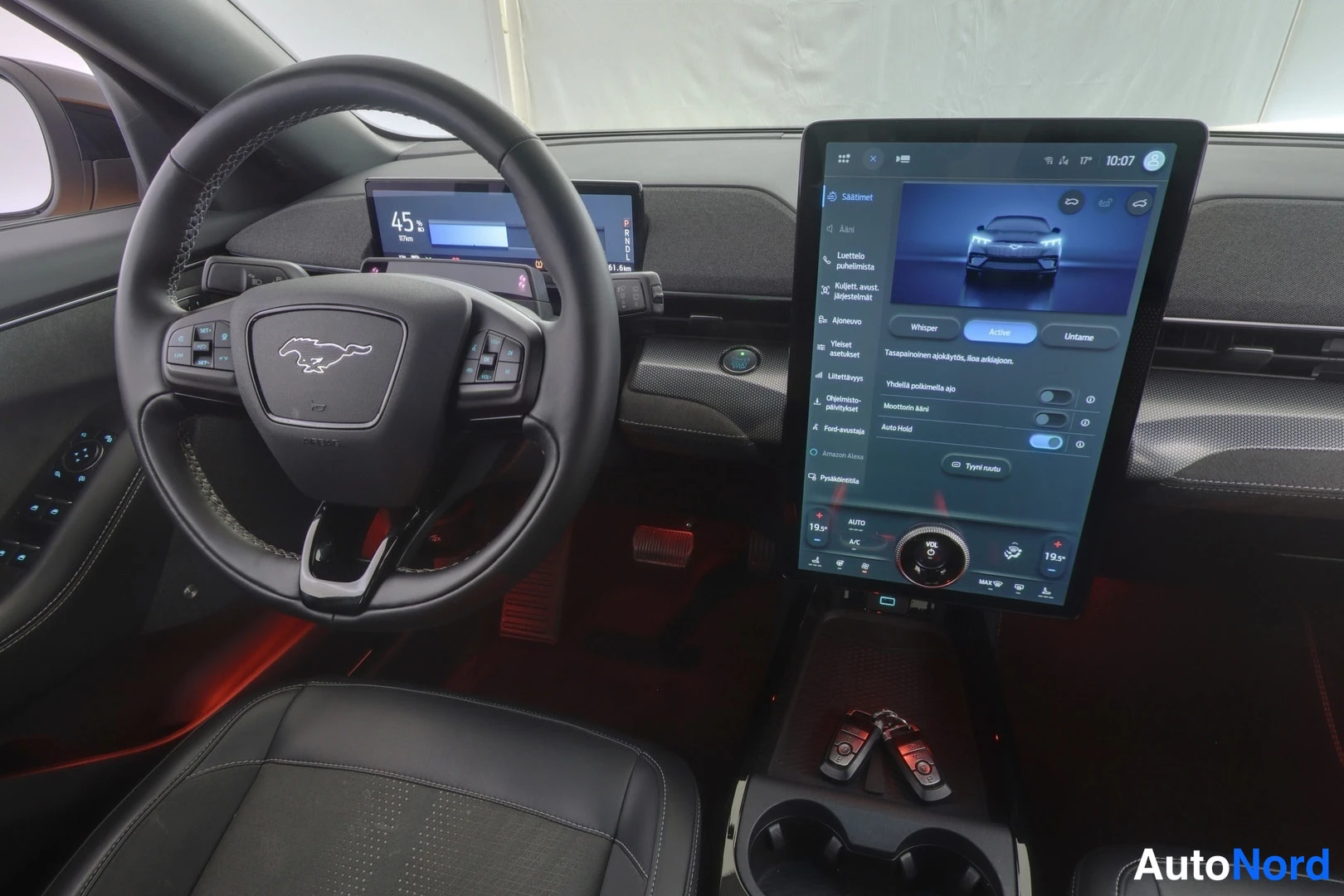 Edestä: Lähikuva Ford Mustang Mach-E:n ohjaamosta: pony-merkkinen ohjauspyörä, kuljettajan näyttö lukemalla 45 km/h ja keskellä pystykosketusnäyttö suomenkielisillä ase