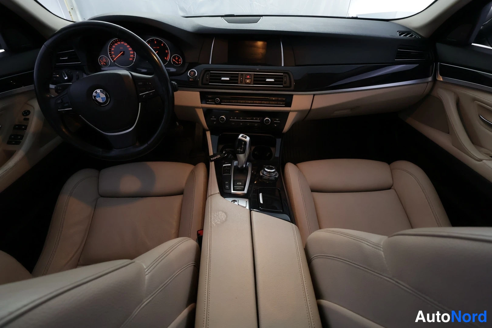Muu: Auton sisätilat etupyöristä: BMW-ohjauspyörä, mittarit, tumma kojelauta ja beige nahkapenkit.