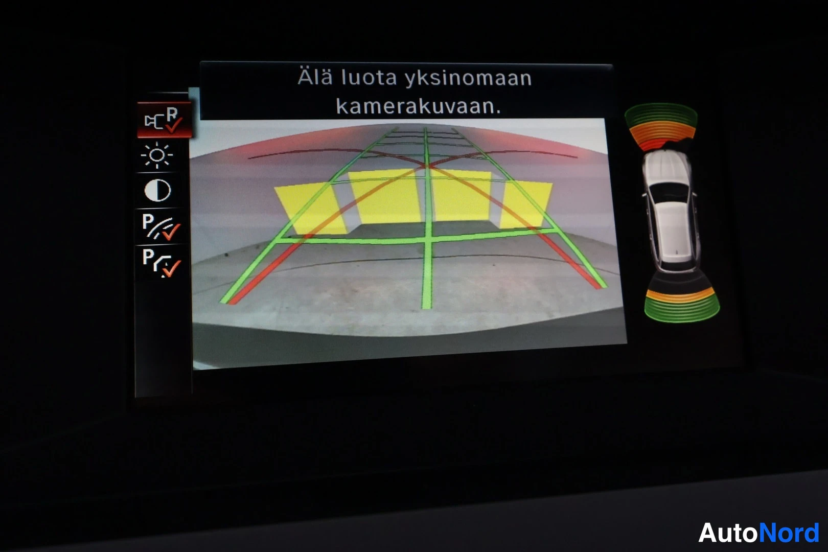 Muu: Auton.infotainment-näyttö näyttää peruutuskameran kuvan ohjausviivoineen ja tekstin Älä luota yksinomaan kamerakuvaan.