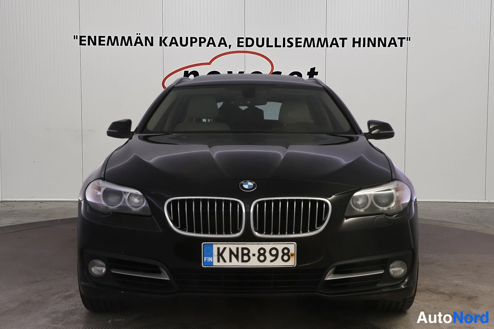 Edestä: Mustan auton suora etunäkymä: etusäleikkö ja ajovalot sekä -rekisterikilpi etupuskissa.