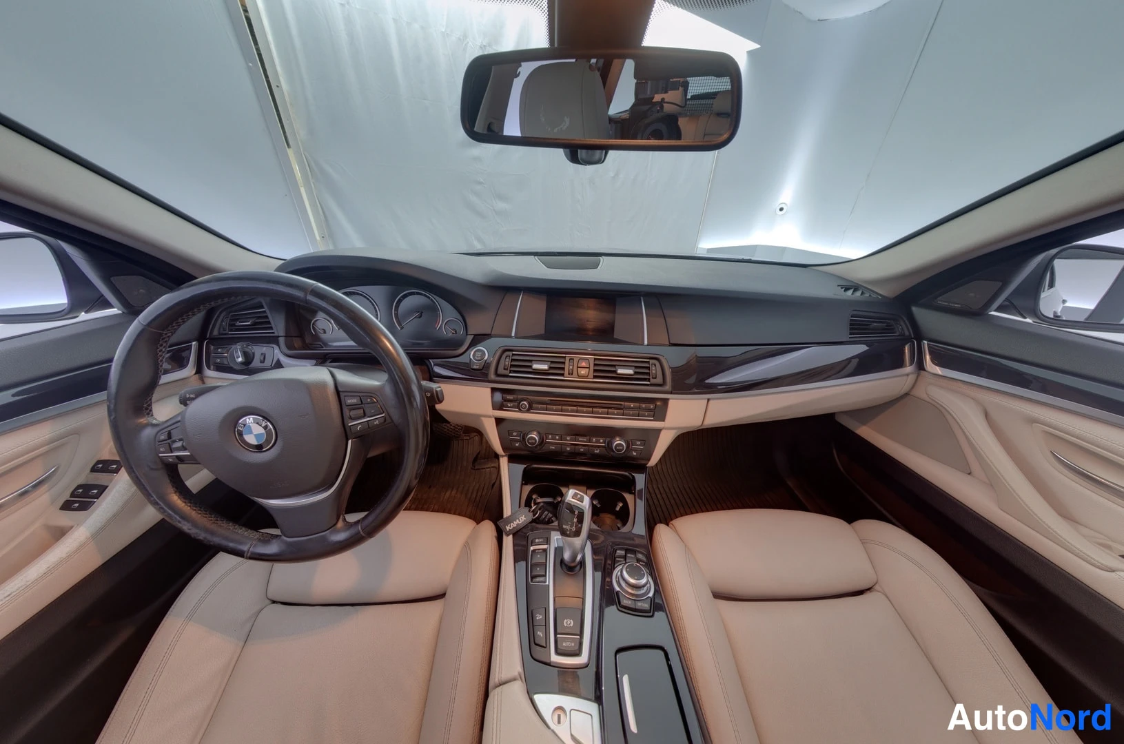 Edestä: Auton sisätilat ohjaamosta: ratissa BMW-merkki, keskikonsolissa vaihtajanappeja ja penkit beigea nahkaa.