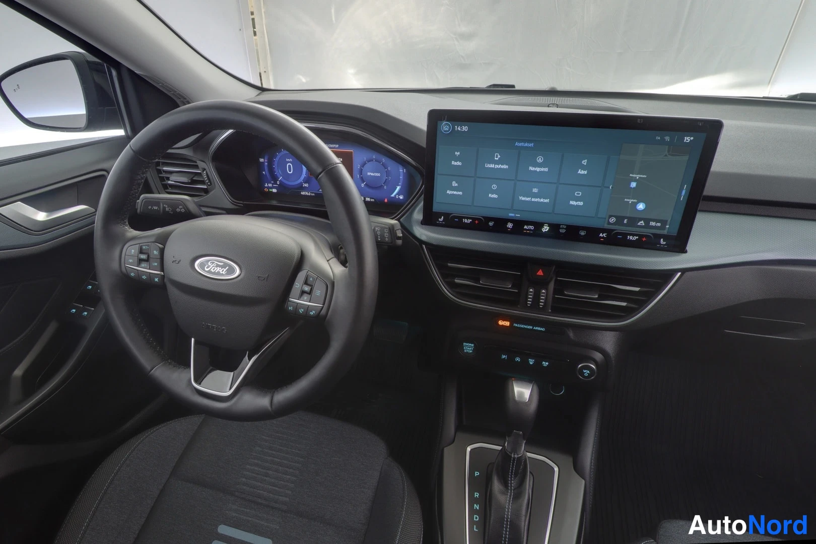 Etuistuimet: Close-up of the driver's area featuring the steering wheel controls, full digital dashboard display showing '0' km/h, and the central infotainment screen displa