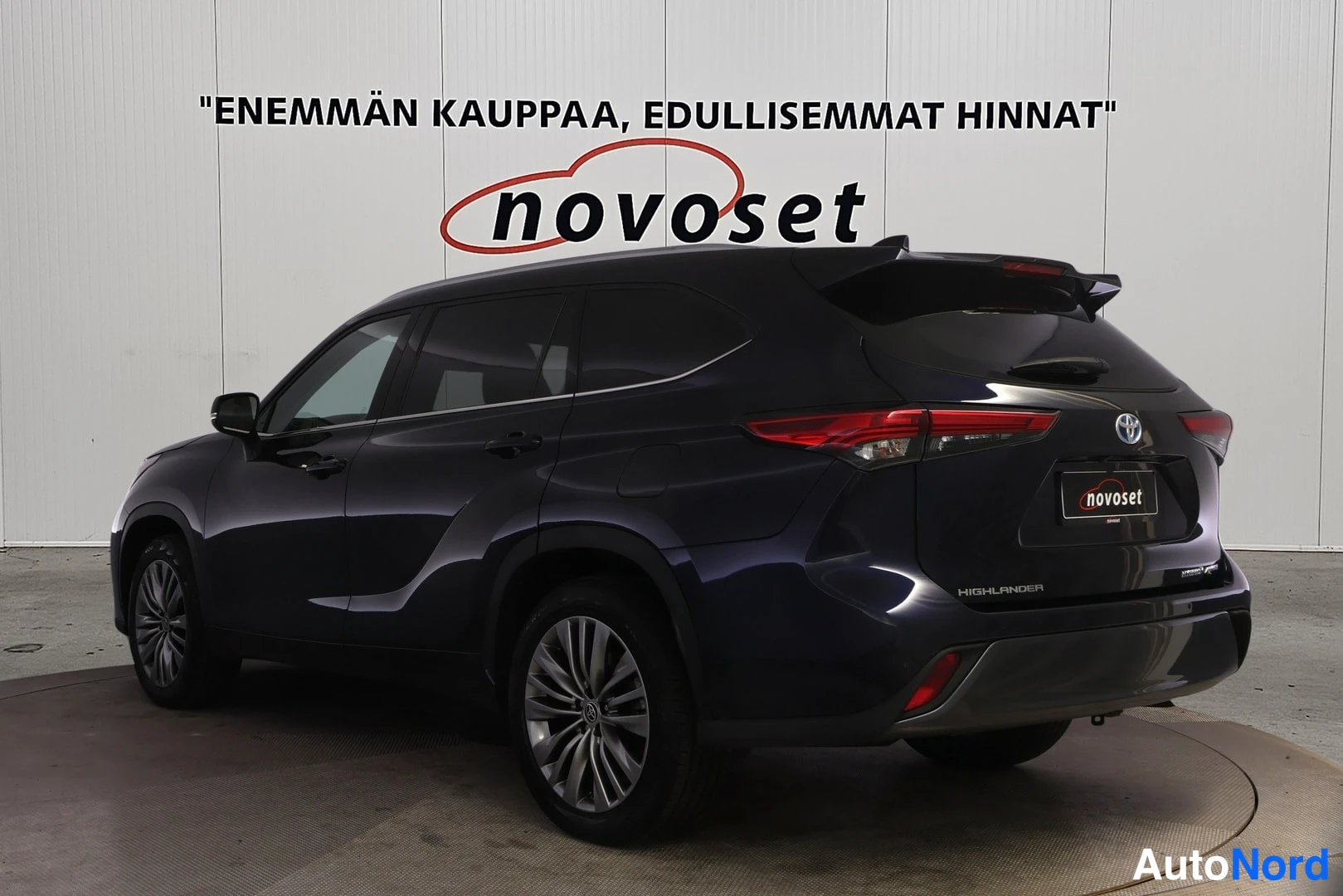 Takaviisto: Toyota Highlanderin takakulmanäkymä takaa ja sivulta, punaiset takavalot ja HIGHLANDER-teksti takapaneelissa.