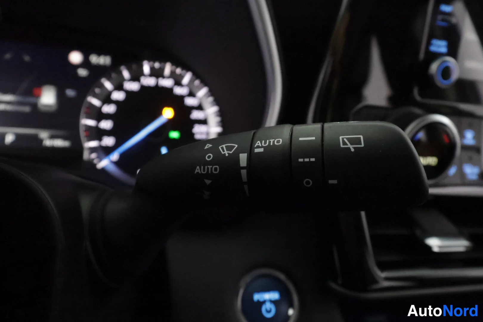 Muu: Sisäkuva: tuulilasinpyyhkimen varsi AUTO-asetuksella, taustalla nopeusmittari ja POWER-käynnistysnappi.
