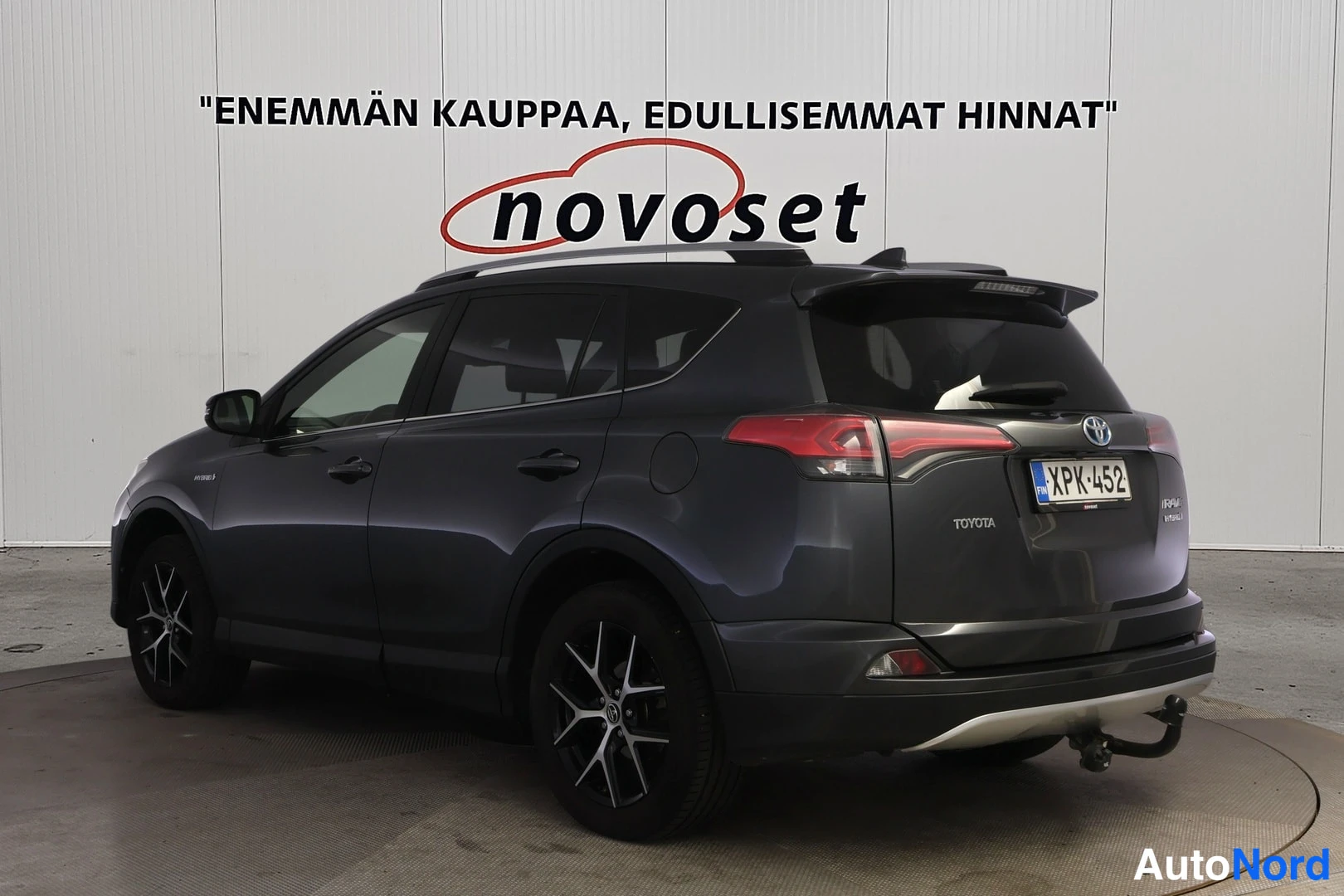 Takaviisto: Tummanharmaa Toyota RAV4 takakolmasosasta; vasen kylki ja takapää näkyvät. Takapuskurin alla vetokoukku, katolla kattokaiteet, pyörissä tummat metallivanteet.