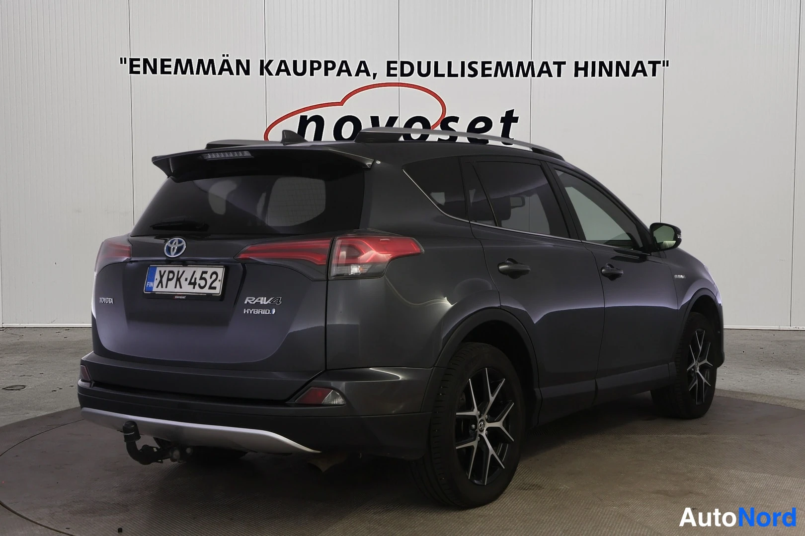 Takaviisto: Tummanharmaa Toyota RAV4 takakolmasosasta oikealta; oikea kylki ja takapää näkyvät. Katolla kattokaiteet, pyörissä tummat metallivanteet, takapuskurin alla veto