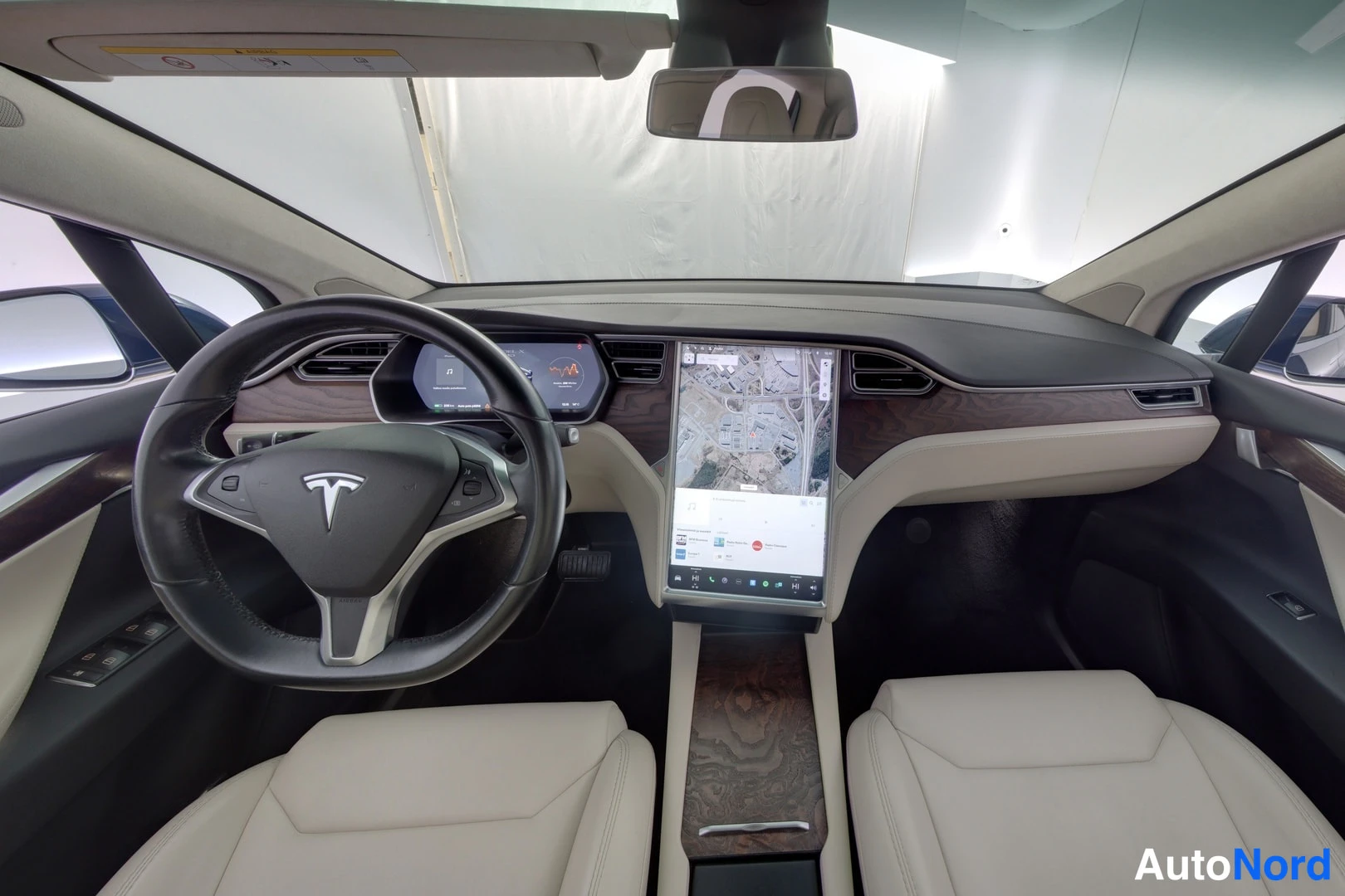 Muu: Tesla-autojen ohjaamo: kuljettajan puolen musta ohjauspyörä Tesla-logolla, keskellä suuri kosketusnäyttö karttanäkymällä, vaaleat istuimet ja tumma kojelauta pu