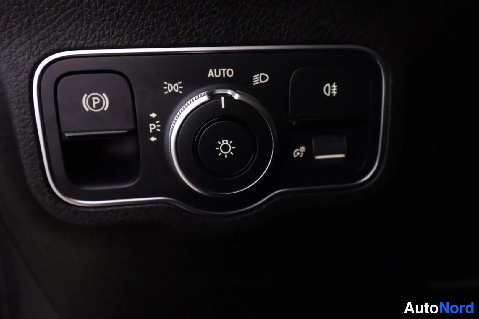 Yksityiskohta: Instrumenttitaulun valonohjainpaneeli, AUTO-asento ja seisontavalot, vasemmalla (P)-painike ja oikealla sumppu- ja kirkasvalo-ominaisuudet.