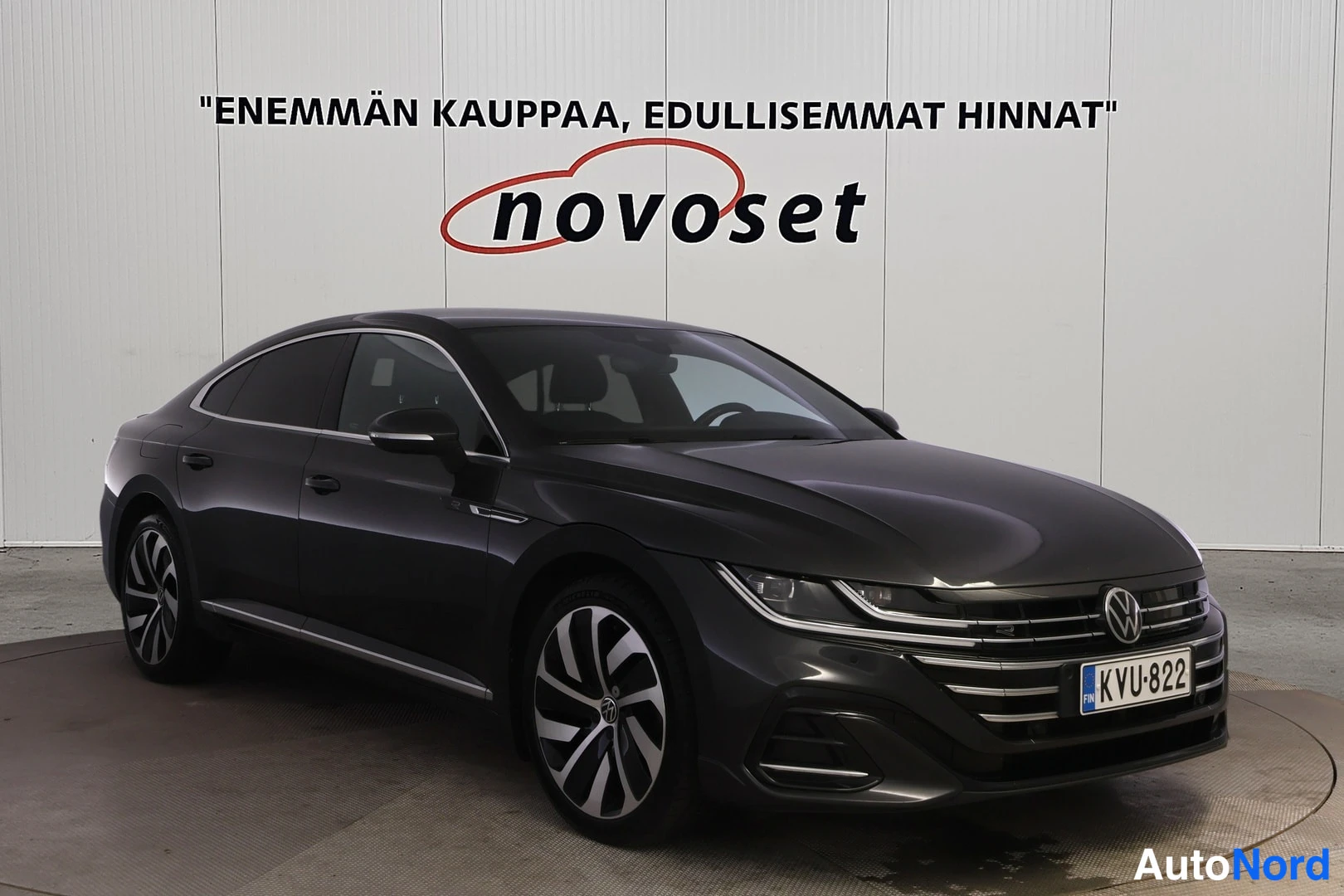 Etuviisto, nokka oikealle: Tummanharmaa Volkswagen Arteon -henkilöauto kolmannesnäkymässä edestä, keula kuvan oikeassa reunassa, rekisterikilpi.