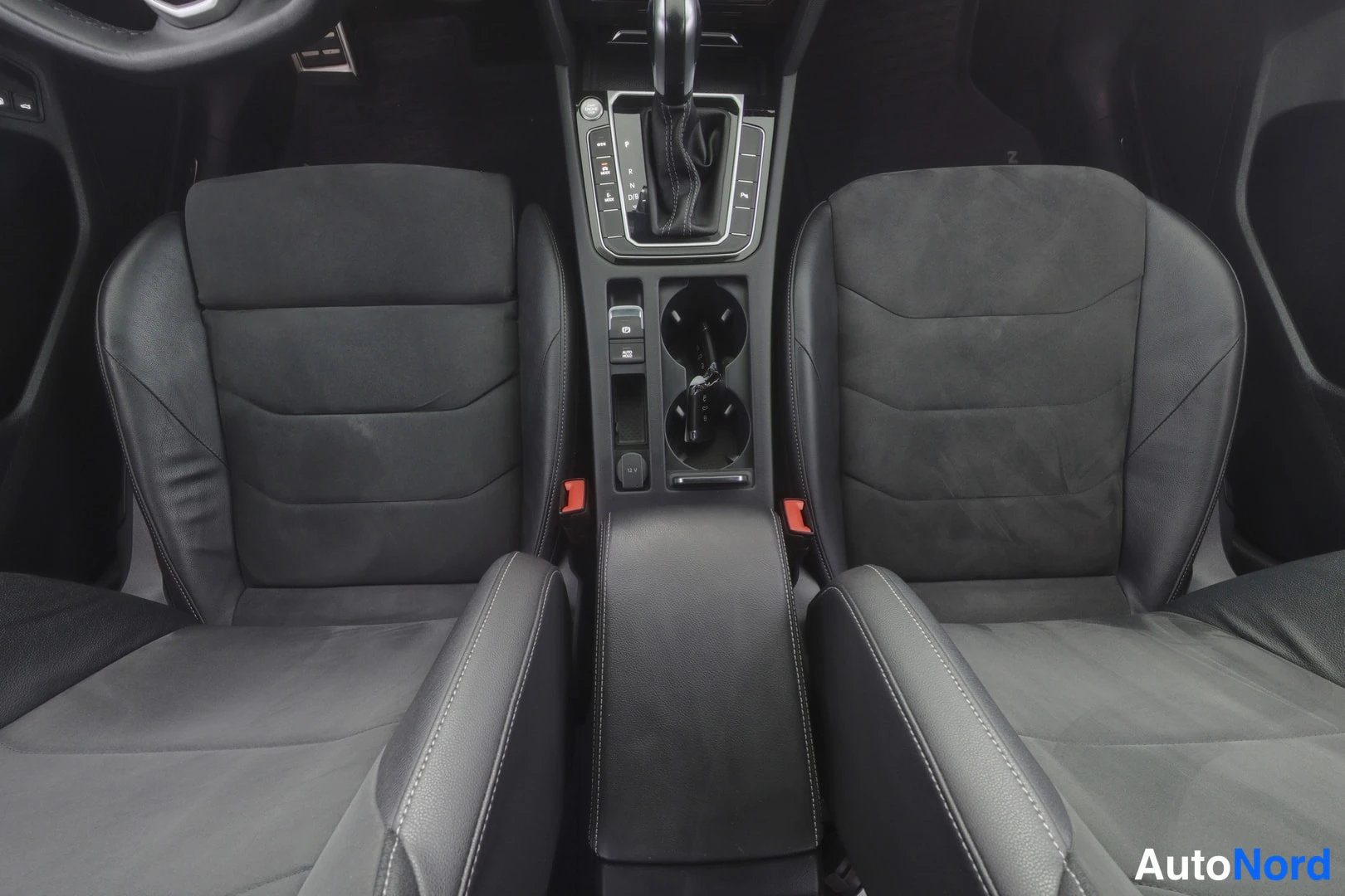 Etuistuimet: Front seats and center console. Two black front seats with leather bolsters and suede-like inserts are seen from a high angle behind the driver's seat. The auto