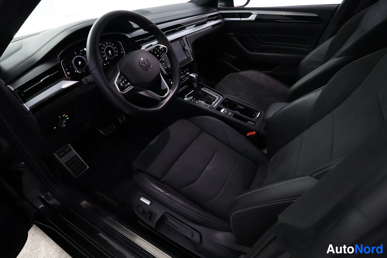 Ohjaamo: Driver's side interior view showing the steering wheel and dashboard. A black multifunction steering wheel with controls is positioned before a digital instrume