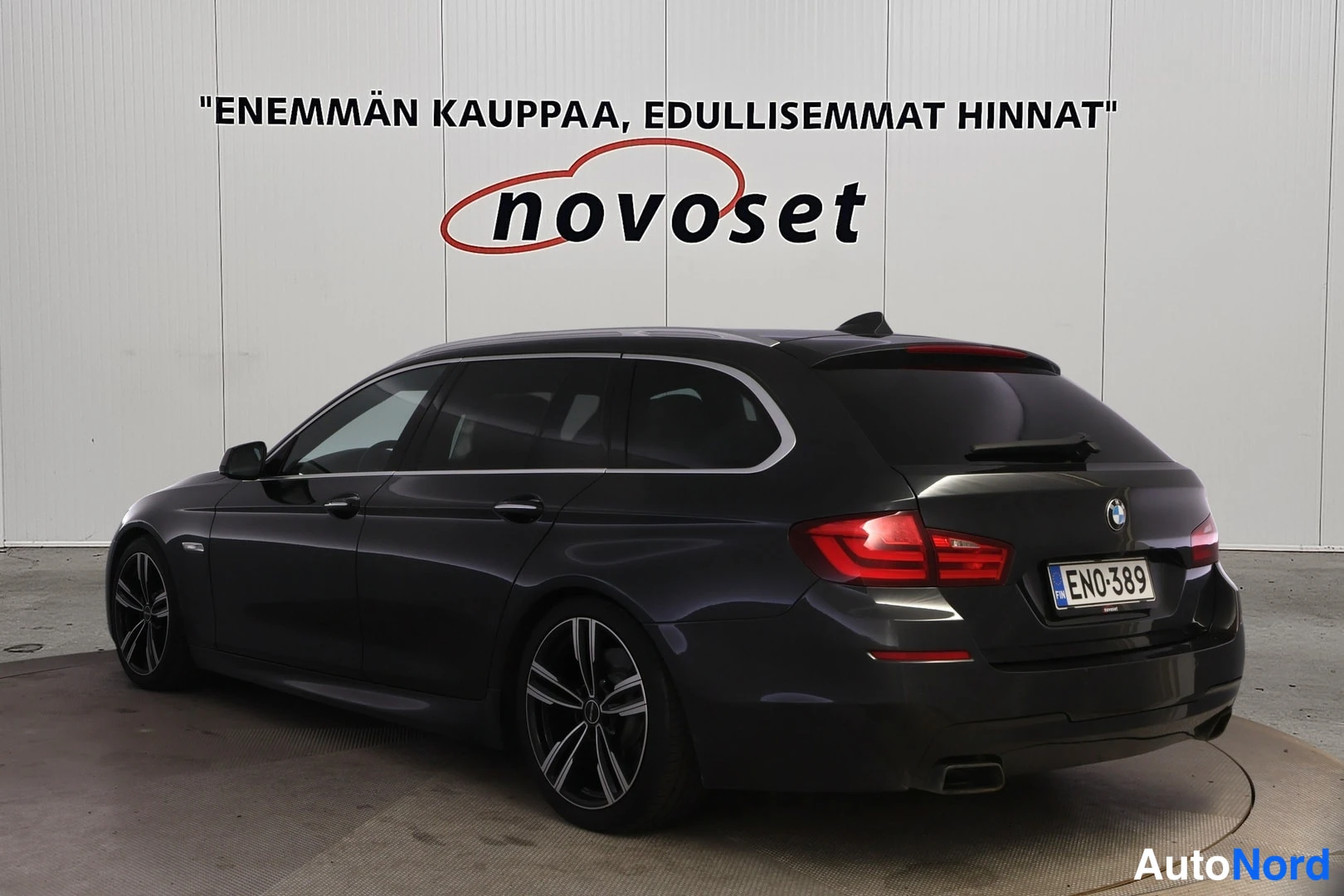 Takaviisto: Tummanharmaa BMW-farmari kuvattuna takakulmasta; takaosa ja vasen kylki näkyvät, takavalojen osa valaisee punaisena, rekisteritunnus.