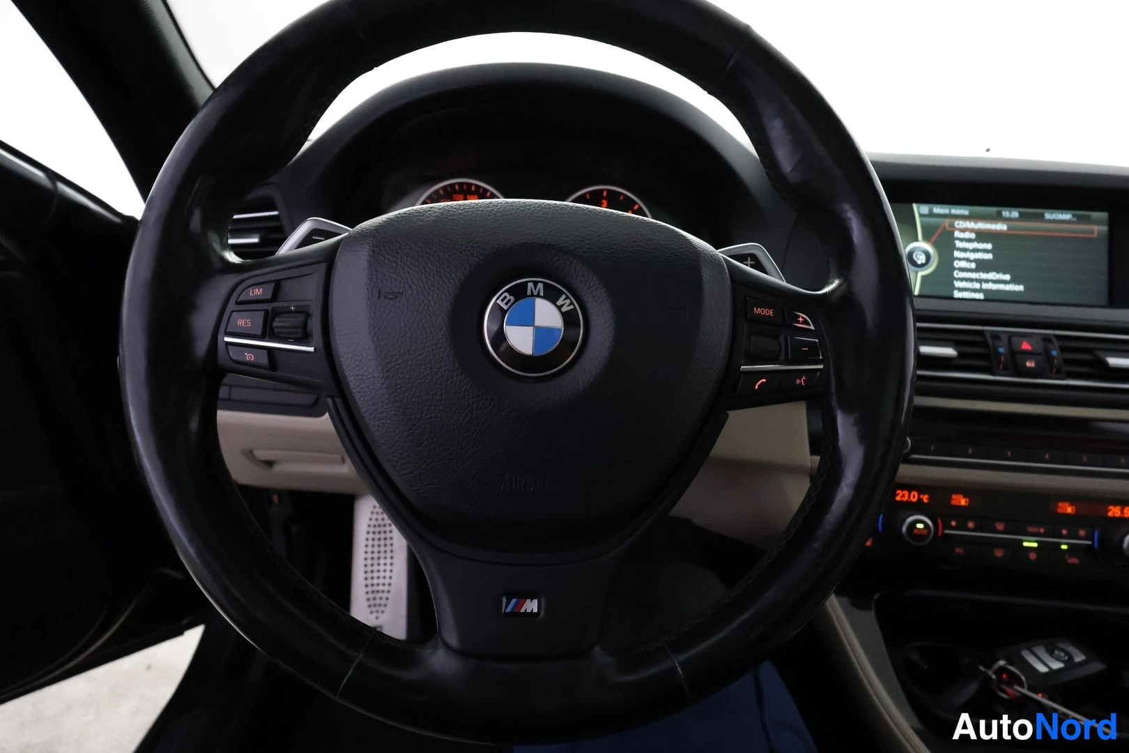 Muu: BMW-merkkinen ohjauspyörä, jossa M-merkki alaosassa; kojelaudan infotainment-näyttö näkyy oikealla.