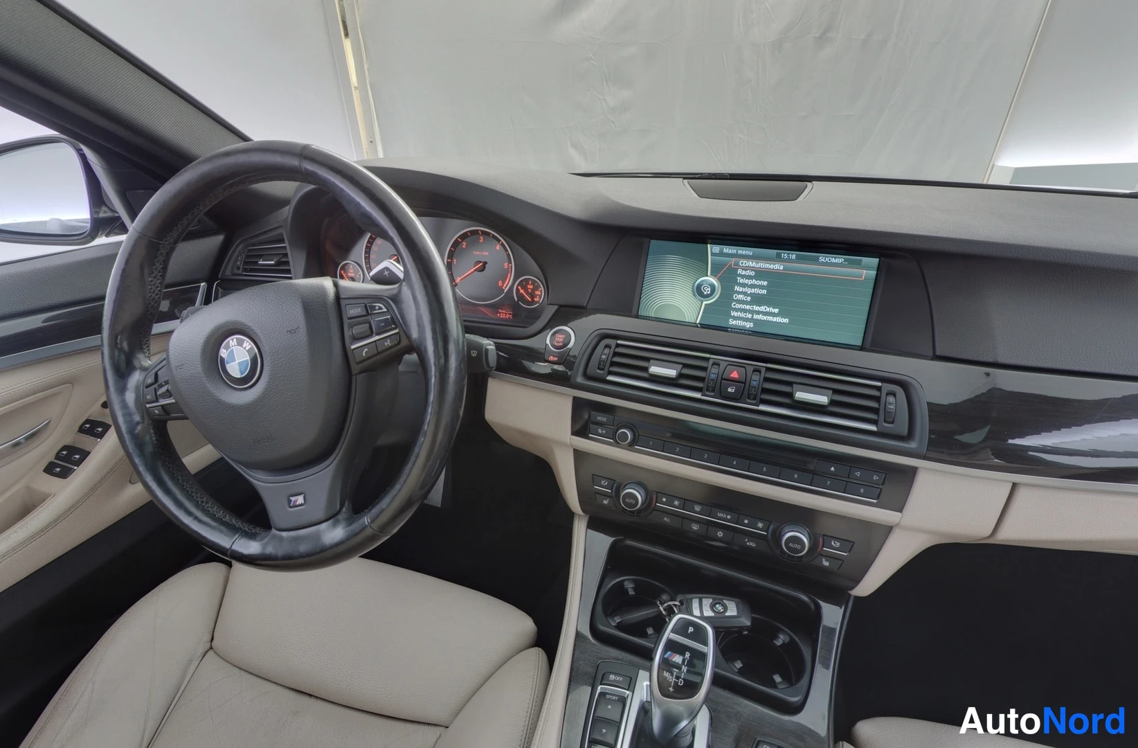 Muu: Lähikuva ohjaamosta: BMW-ohjauspyörä, mittaristo ja iDrive-näyttö, jossa COMMUNICATION-valikko (Radio, Media, Navigation, Office, ConnectedDrive), sekä automaat