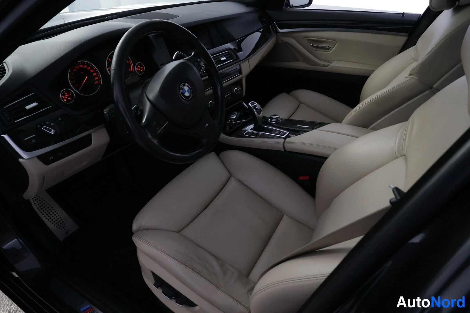 Ohjaamo: Ohjaamo etuosasta: musta BMW:n ohjauspyörä, tumma instrumenttikeila kelloineen sekä beigen sävyiset verhoilut.