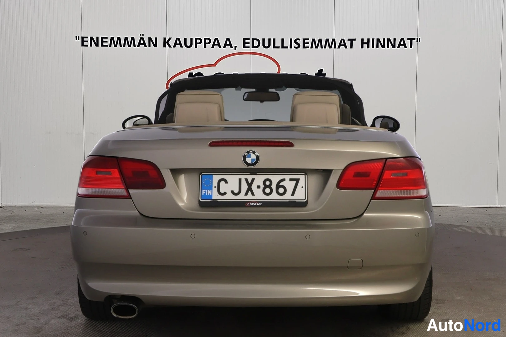 Takaa: Direct rear view of the gold convertible showing the trunk lid, dual taillights, and single exhaust pipe on the left side. The beige seats are visible behind th