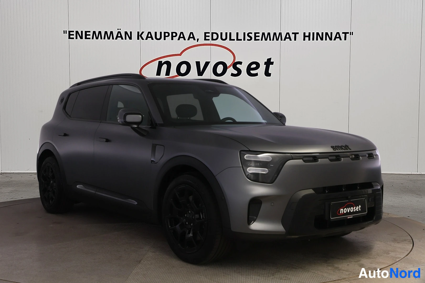 Etuviisto, nokka oikealle: Tummanharmaa Smart-henkilöauto etuviistosta oikealta; mustat vanteet, kattokaiteet ja smart-merkki konepellissä.