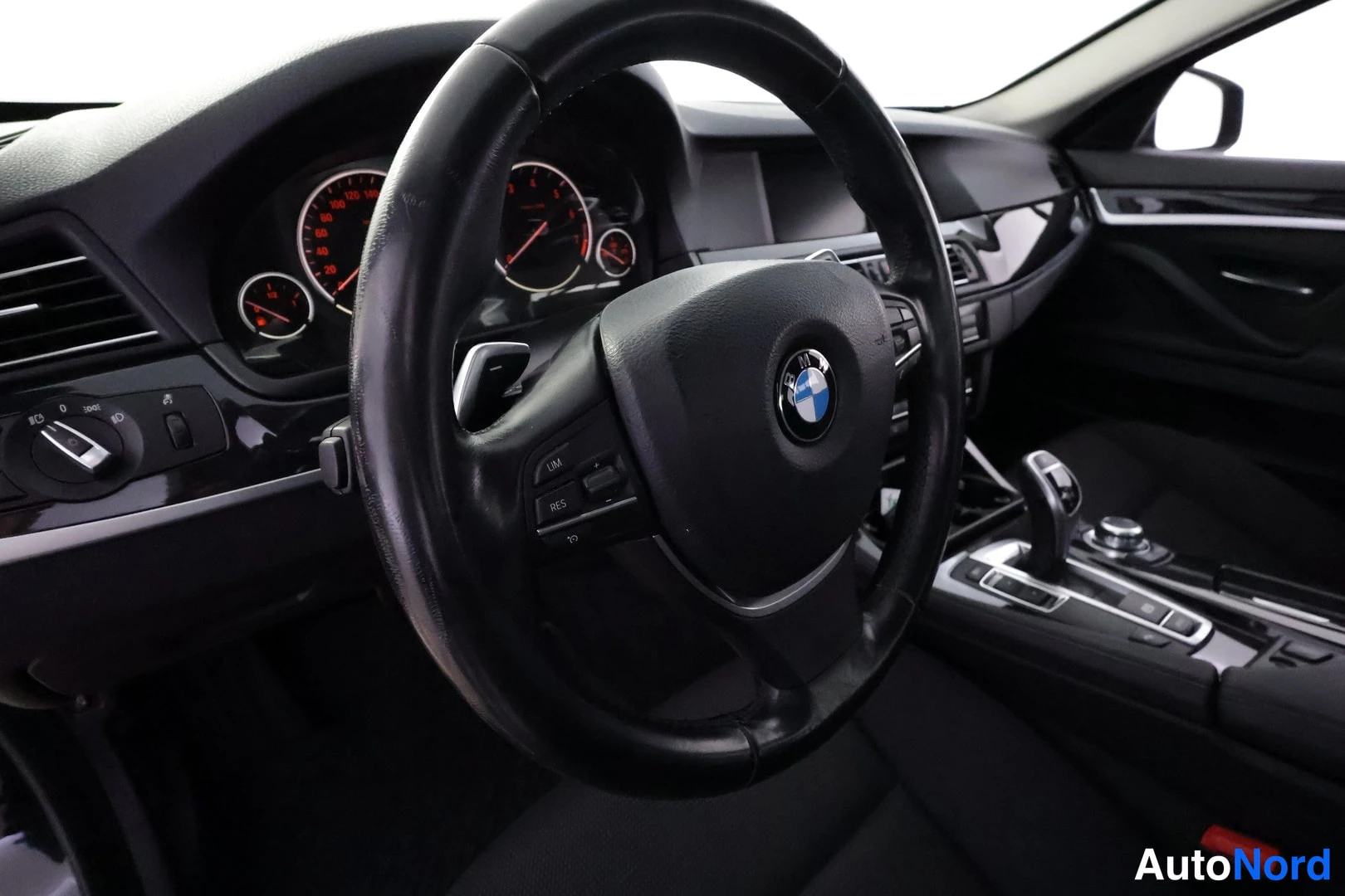 Sivulta: Sisäkuva: BMW-ohjauspyörä, punataustaiset mittarit ja keskikonsolin vaihtokeksi ja säätimet