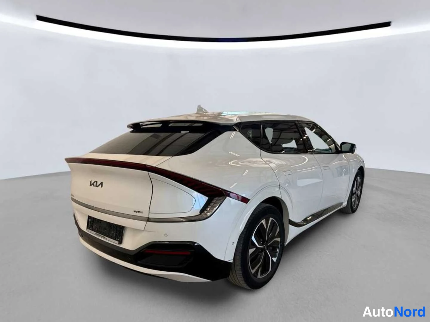 Takaviisto: KIA EV6 takaapäin vasemmalta: valkoinen korirakenne, Kia-merkki takaluukussa, kulmikkaat takavalot ja tummat pyörät studiossa.