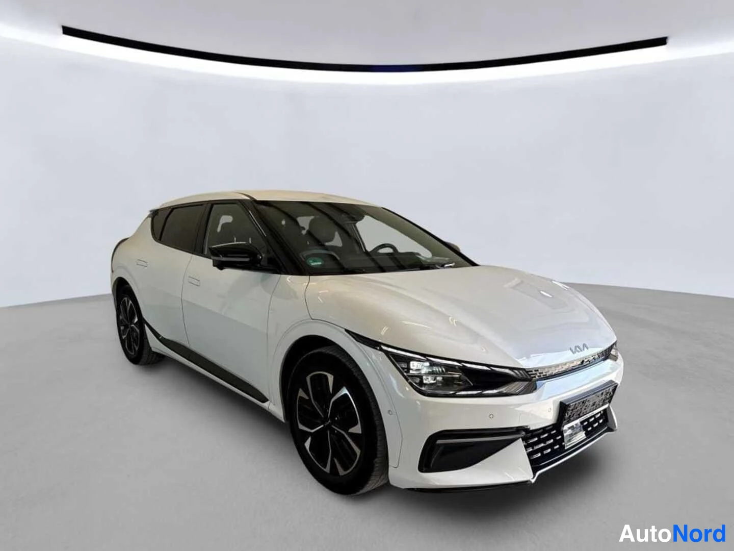 Etuviisto, nokka oikealle: KIA EV6 etunäkymä oikealta edestä: valkoinen korirakenne, Kia-merkki etusäleikössä, terävät etuvalot ja tummat monirunkovanteet studiossa.