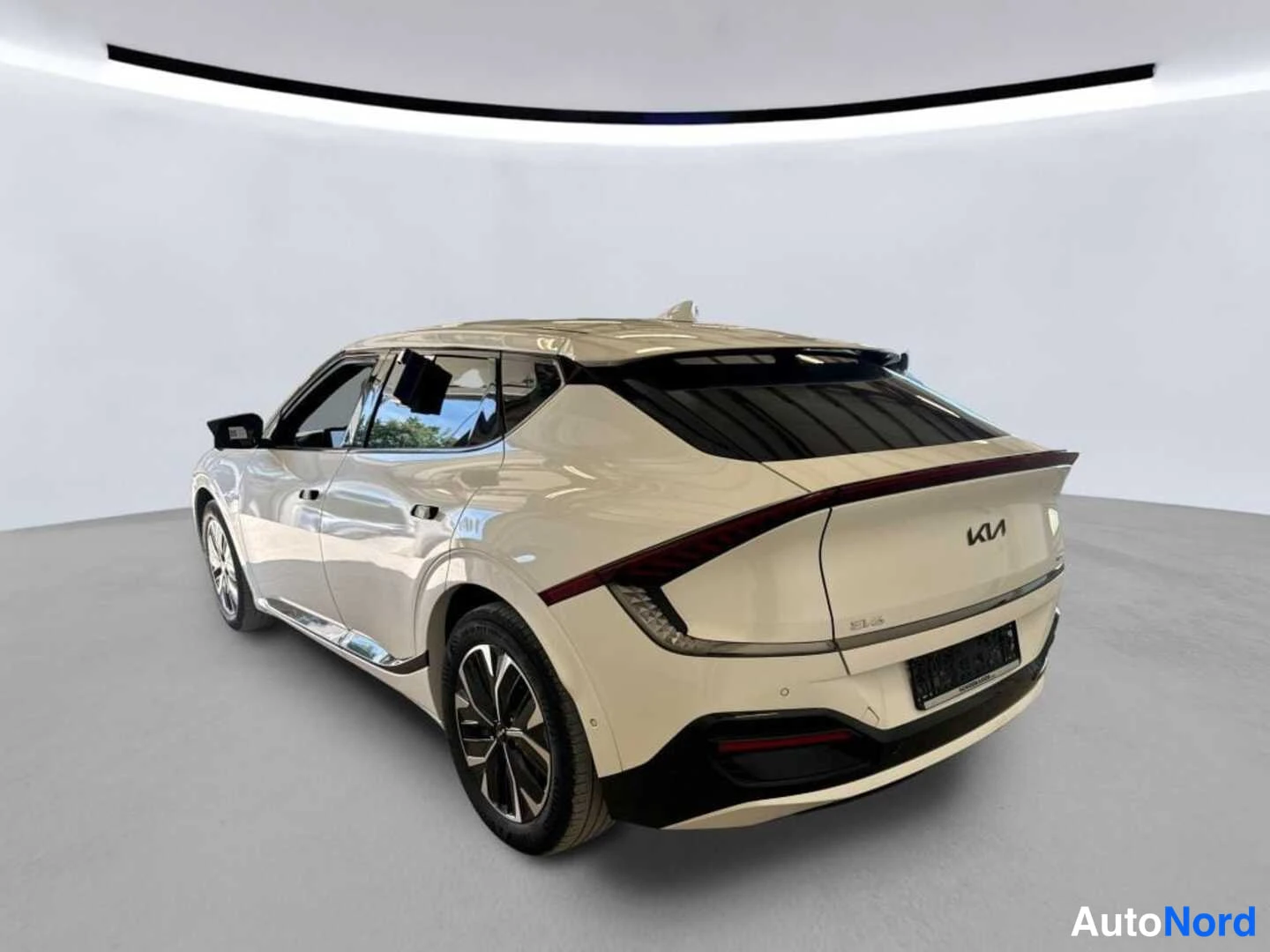 Takaviisto: KIA EV6 takaapäin oikealta: valkoinen korirakenne, Kia-merkki takaluukussa, kulmikkaat takavalot ja tummat pyörät studiossa.