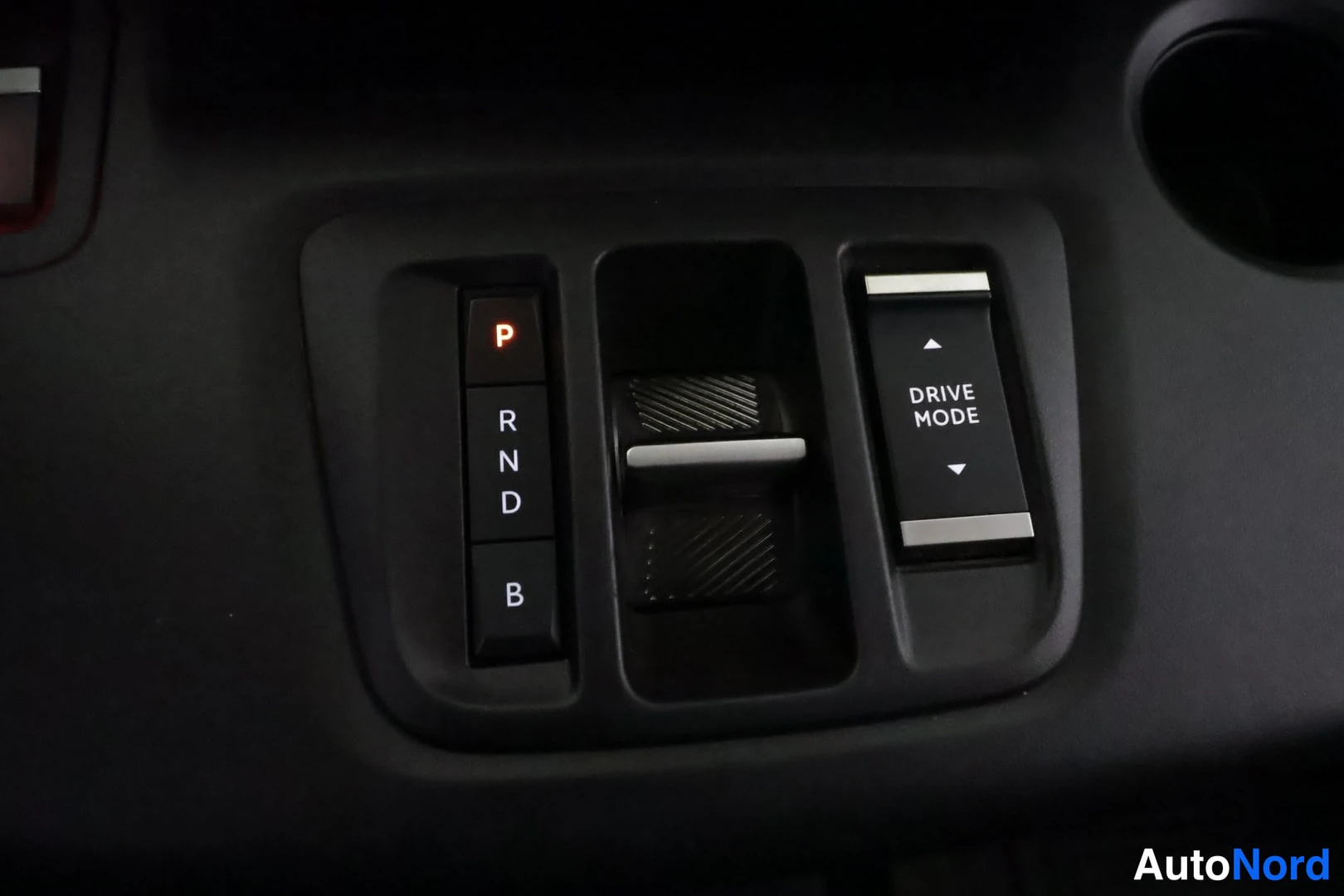 Muu: Lähikuva keskikonsolin vaihtopainikkeista: punaisesti valaistu P, alapuolella R, N, D ja B, sekä DRIVE MODE-kytkin nuoline.