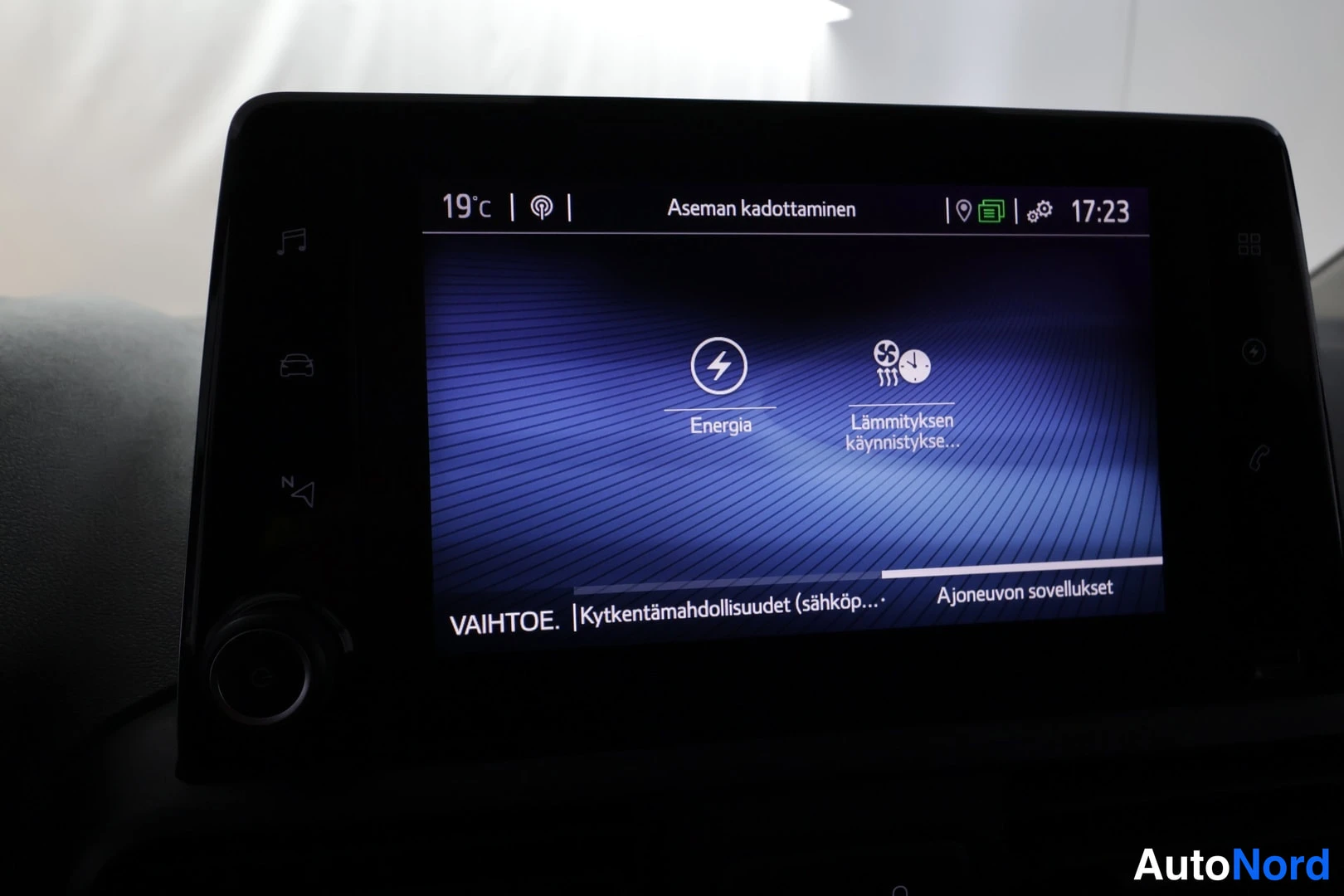 Muu: Auton infotainment-näytön Energia-valikko, jossa vaihtoehdot Energia ja Lämmityksen käynnistys; yläpalkissa 19 °C ja kello 17:23.