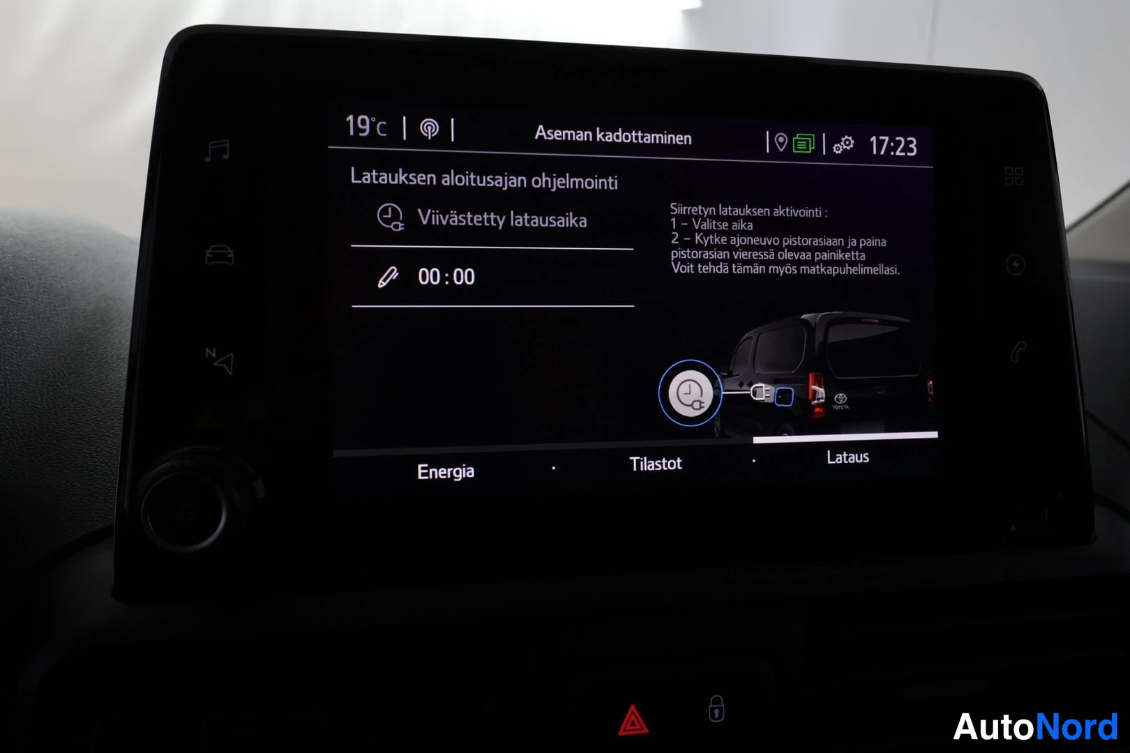 Muu: Auton infotainment-näytön Lataus-sivu, jossa ohjelmoidaan latauksen aloitusaikaa; näkyy 'Viivästetty latausaika 00:00' ja latausohje.