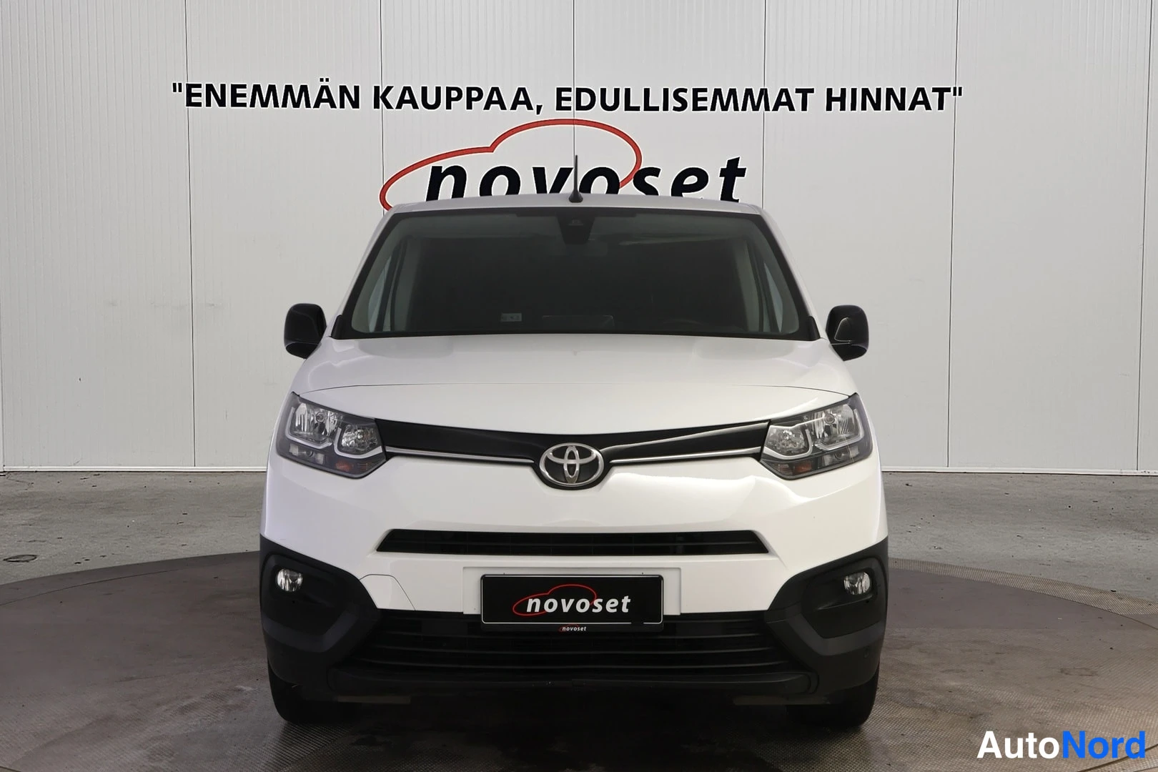 Edestä: Valkoinen Toyota-auto, joka seisoo suorassa edestä. Takapaino peilaa valoa