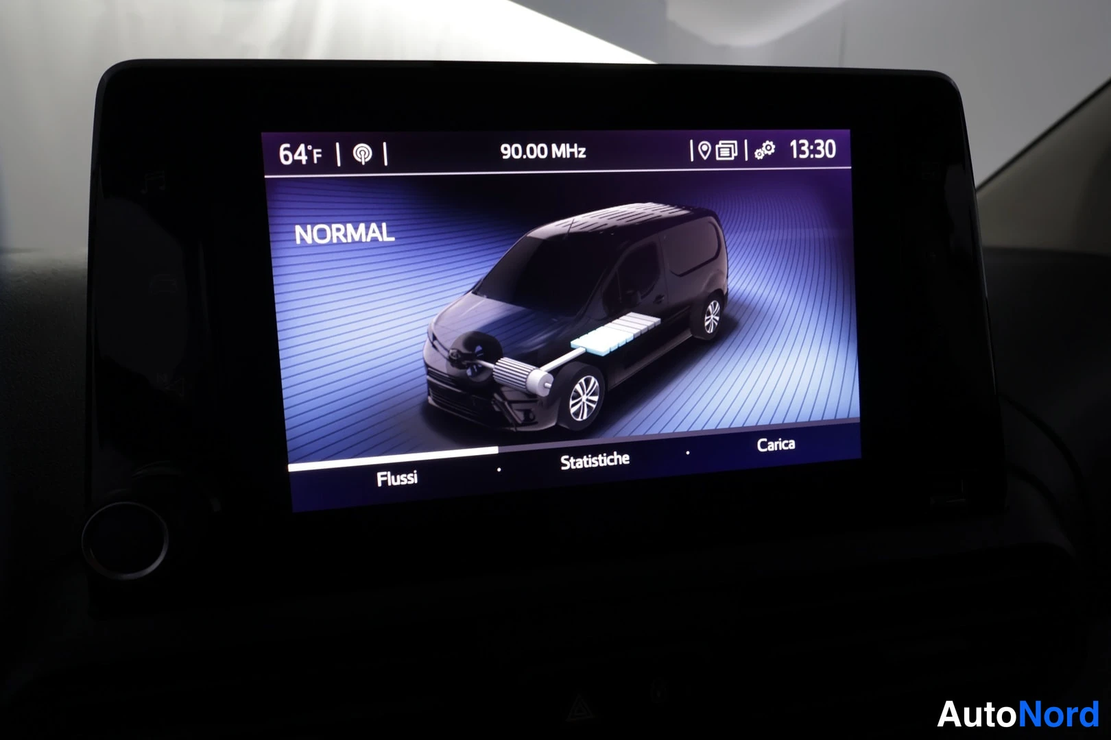 Muu: Kojelaudan kosketusnäyttö, jossa näkyy radio 90.00 MHz ja sähköautoa kuvaava energia-näkymä NORMAL-tilassa sekä alavalikot Flussi, Statistiche ja Carica.