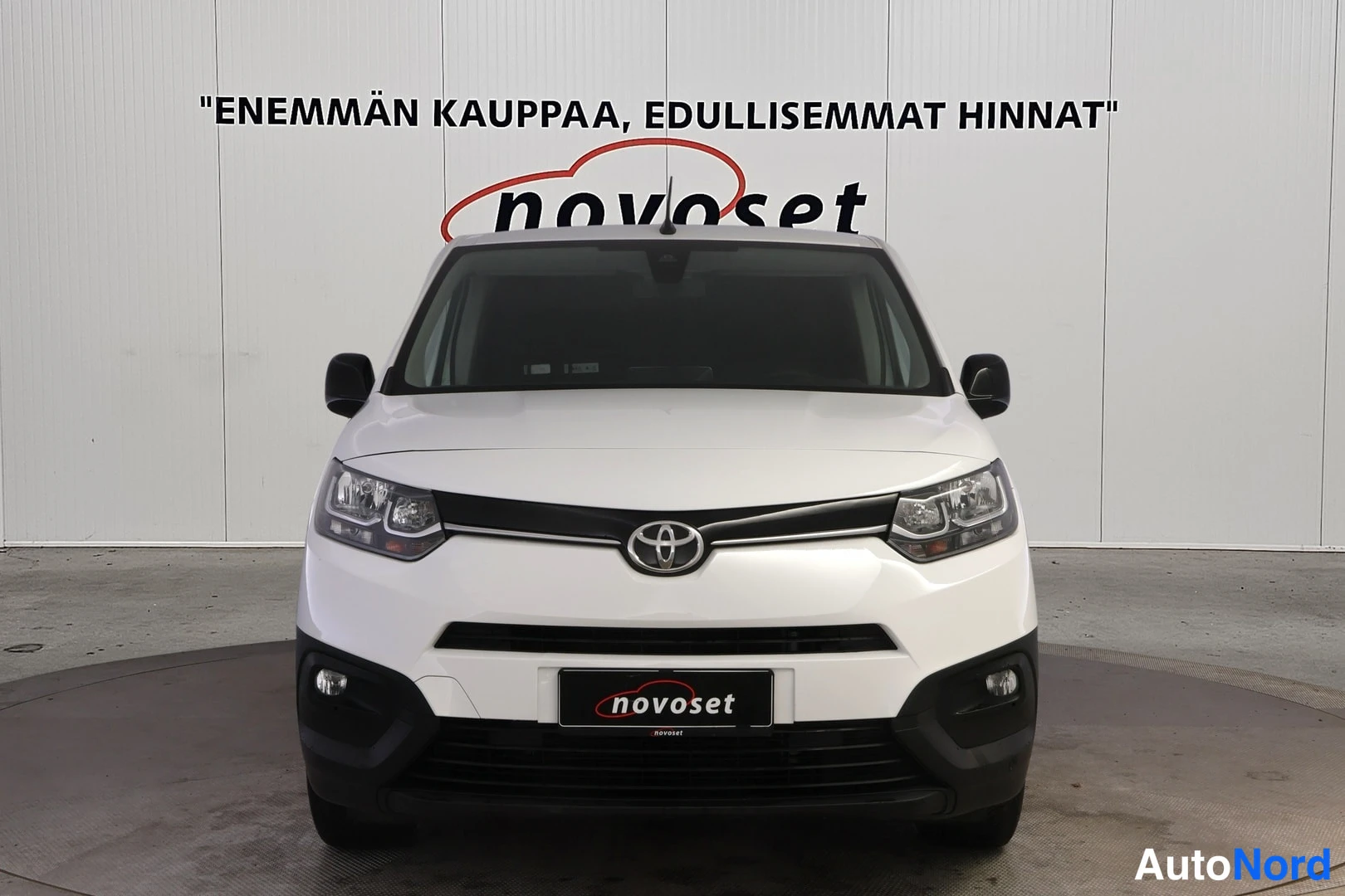 Edestä: Valkoisen Toyota Proace City -pakettiauton suora etunäkymä, Toyotan merkki mustassa säleikössä, novoset-tunnus rekisterikilven paikalla.