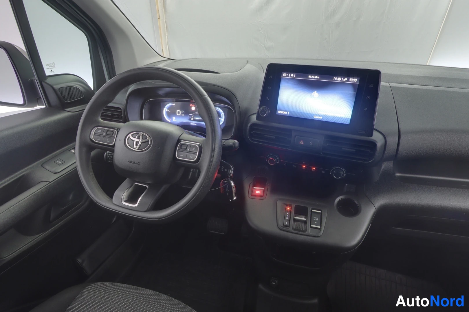 Muu: Sivulta kuvattu Toyota Proace Cityn ohjaamo: ohjauspyörä napeilla, digitaalinen mittaristo, kosketusnäyttö ja vaihdevalitsimet keskikonsolissa.