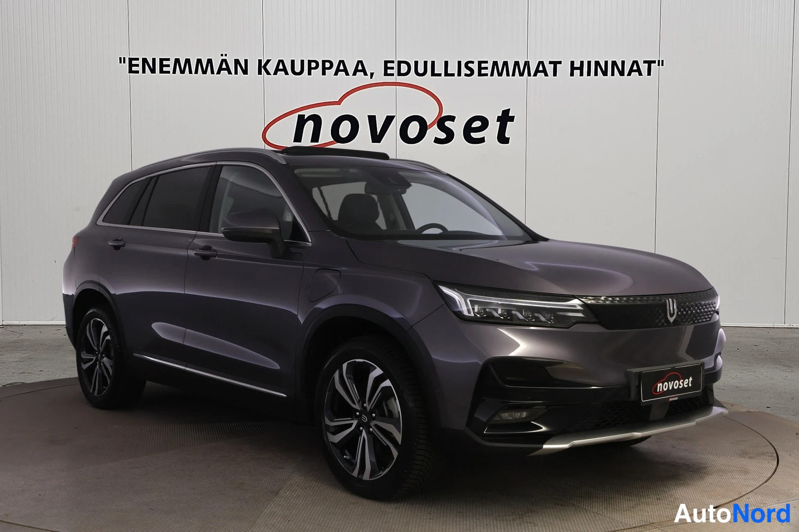 Etuviisto, nokka vasemmalle: Front three-quarter view of a dark grey Skywell SUV with black roof rails and two-tone alloy wheels