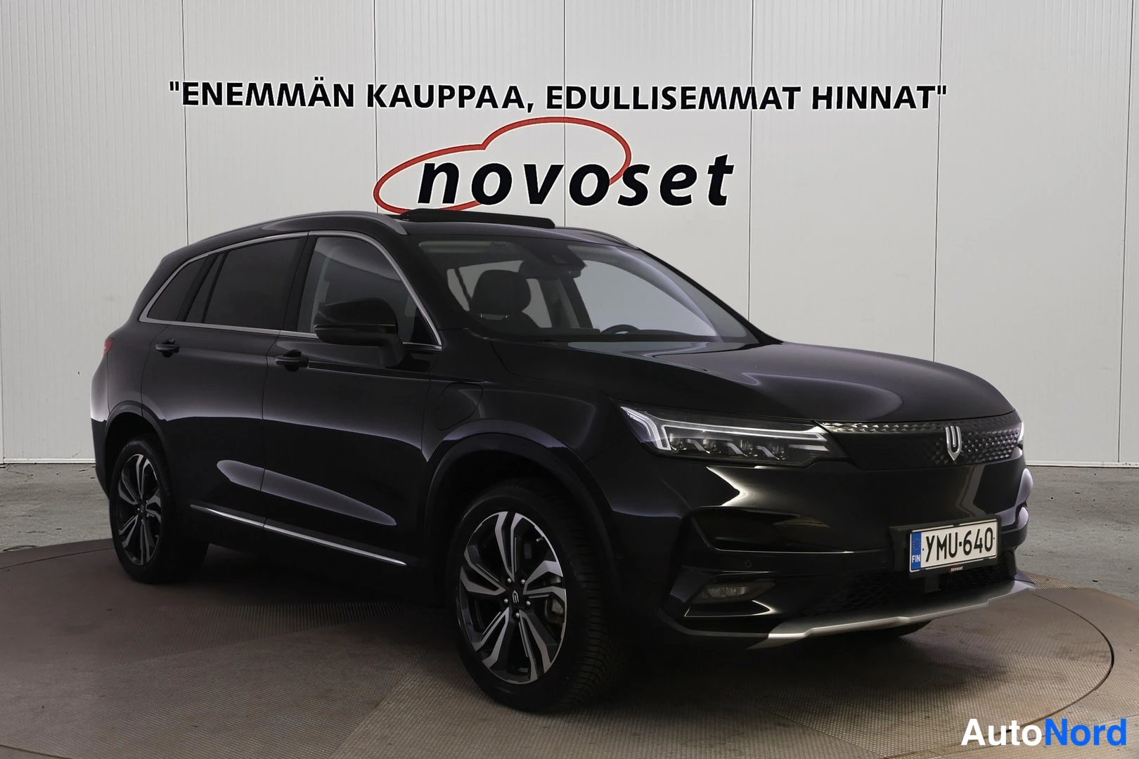 Etuviisto, nokka oikealle: Musta SUV etuviistosta oikealta kuvattuna sisätiloissa; keula ja vasen kylki näkyvät, rekisterikilpi, monipuoliset alumiinivanteet, taustalla valkoinen s