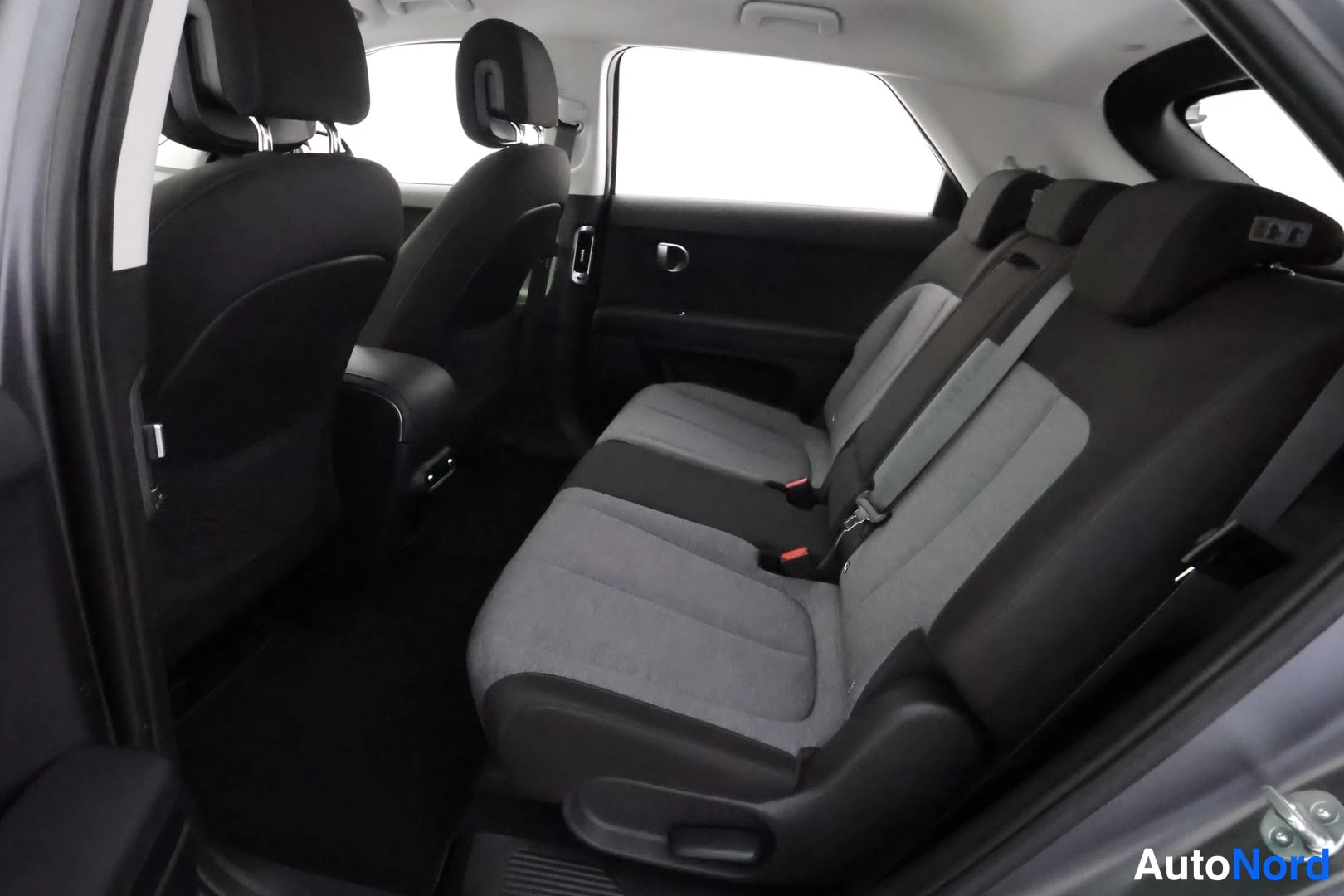 Takaistuimet: Back seat interior with black and grey fabric upholstery, showing two out of three rear seats, door panel and window.