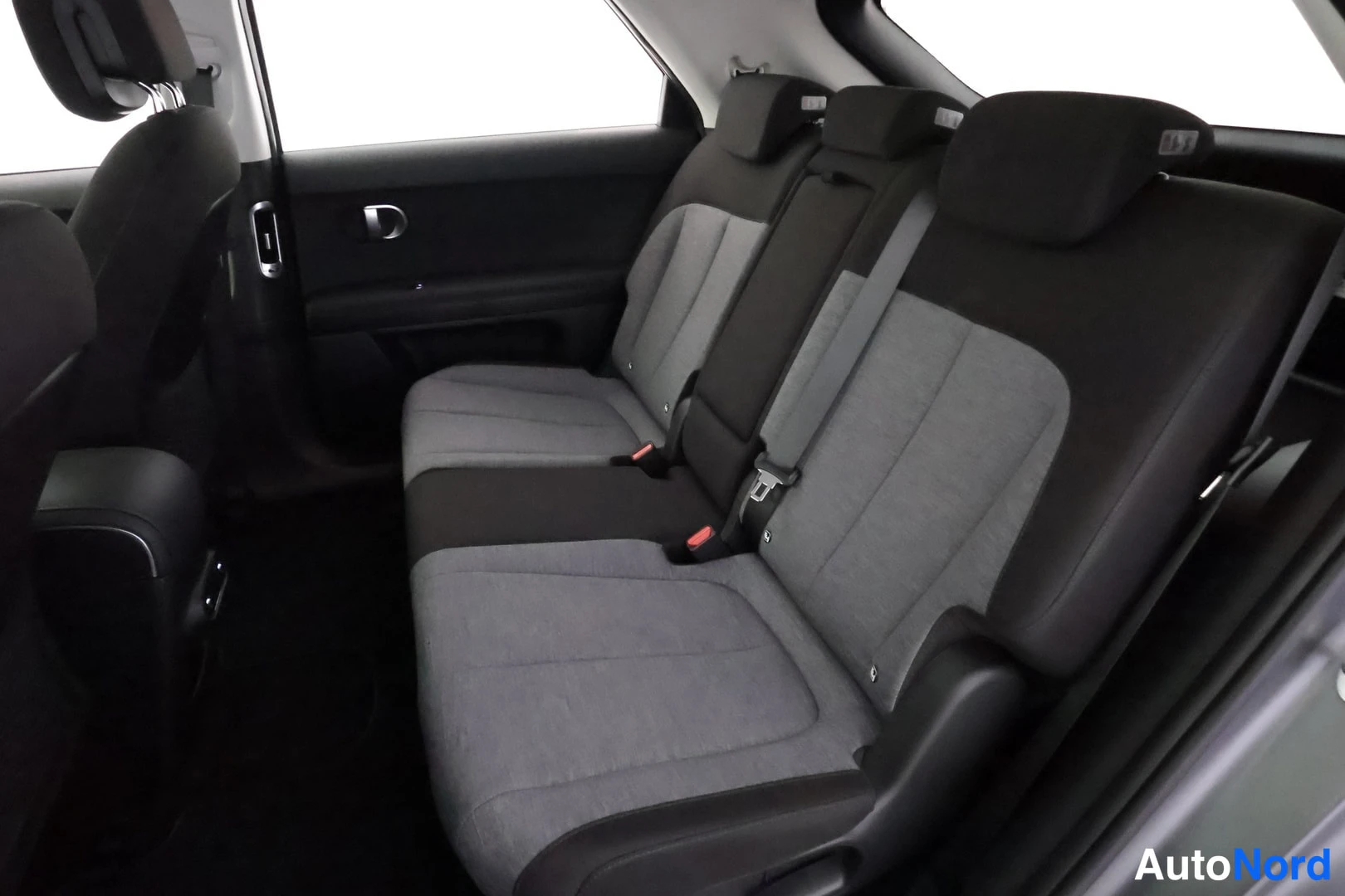 Takaistuimet: Rear passenger area with three-seat bench in dark grey and light grey fabric, including headrests, seatbelts, door handle and trim.