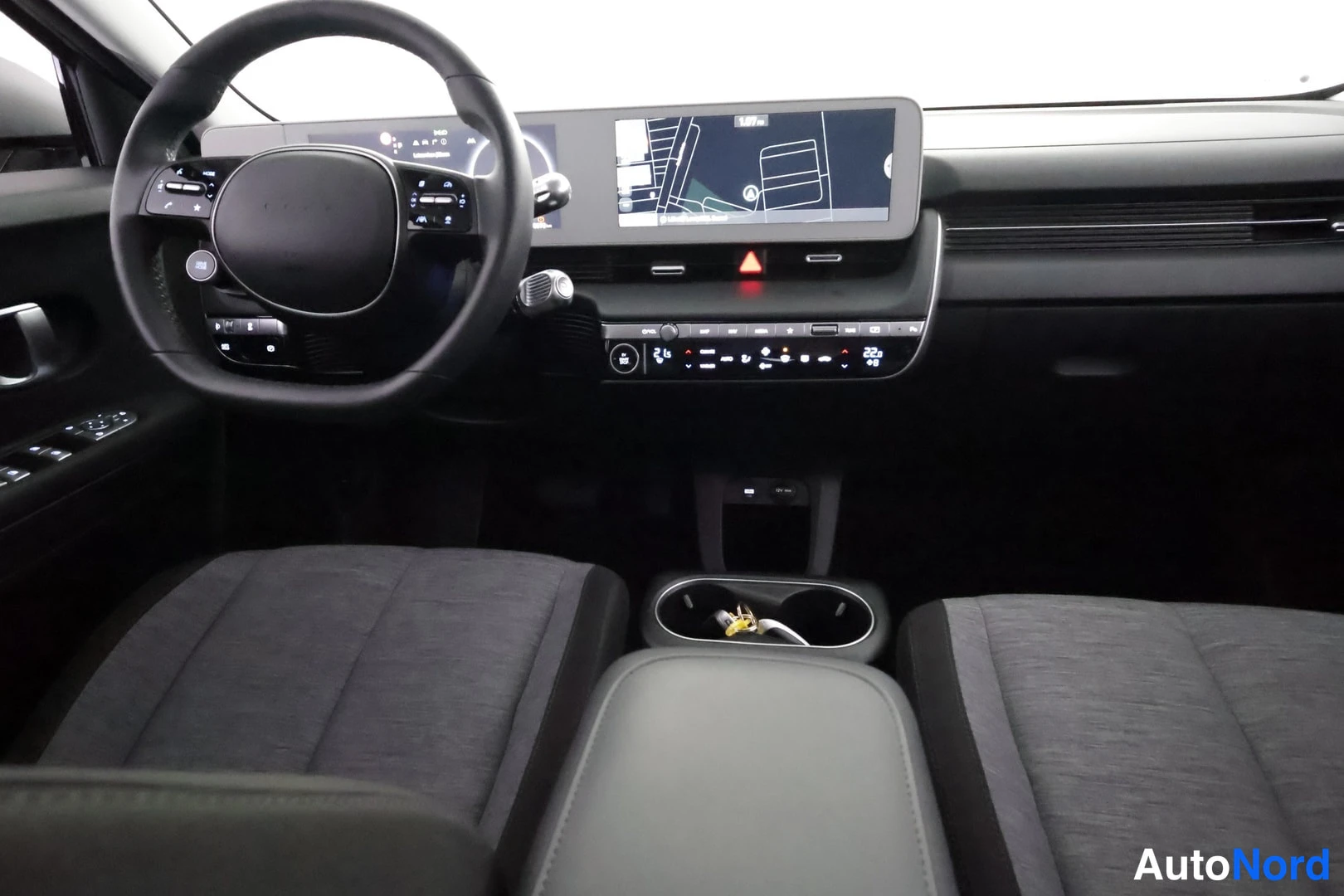 Etuistuimet: Interior shot from rear perspective looking forward, showing dashboard screens, steering wheel, gear selector console and front seats.