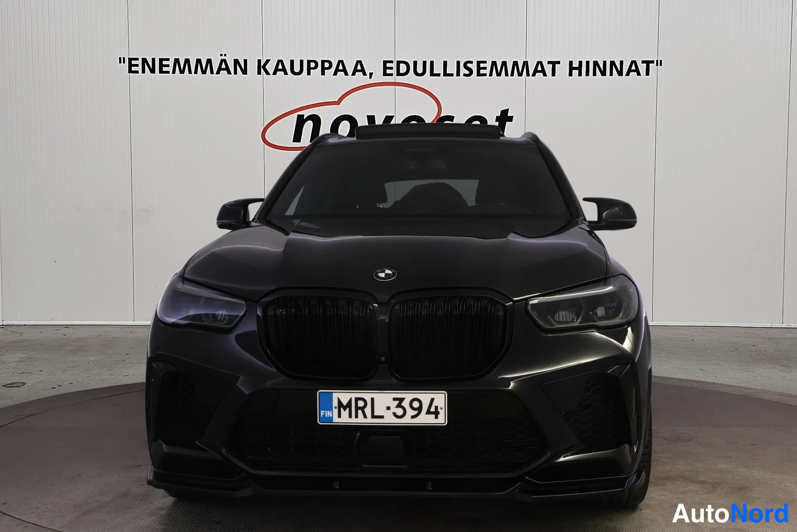 Edestä: Musta BMW X5 suoraan edestä kuvattuna, munuaisjärisäleikkö, ajovalot ja etupuskurin recurkeleke näkyvät, rekisteritunnus.