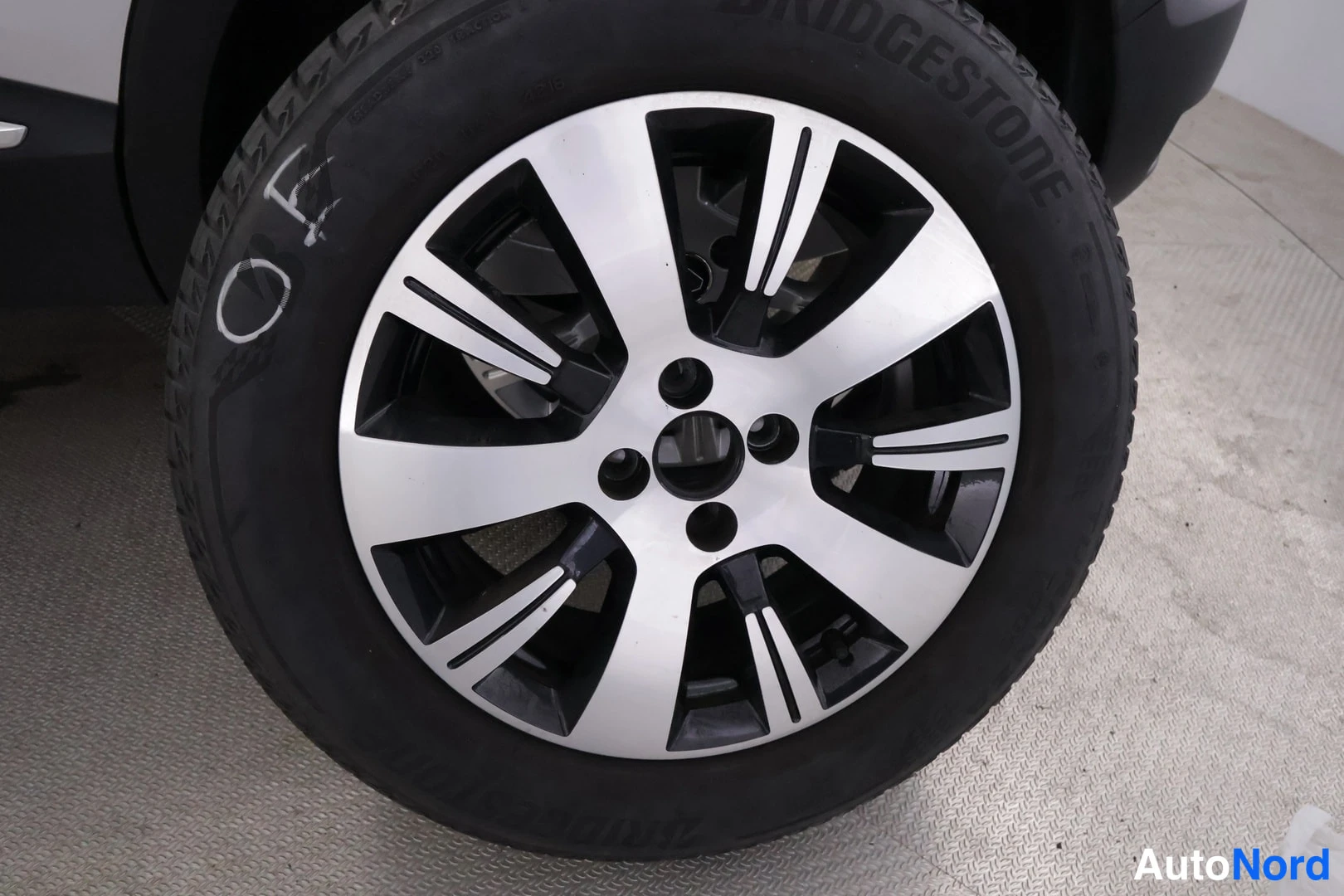 Yksityiskohta: Renkaiden Bridgestone-renkuksen ja kaksivärin alumiinivanteen lähipika, renkaaseen on kirjoitettu valkoisella merkintä.