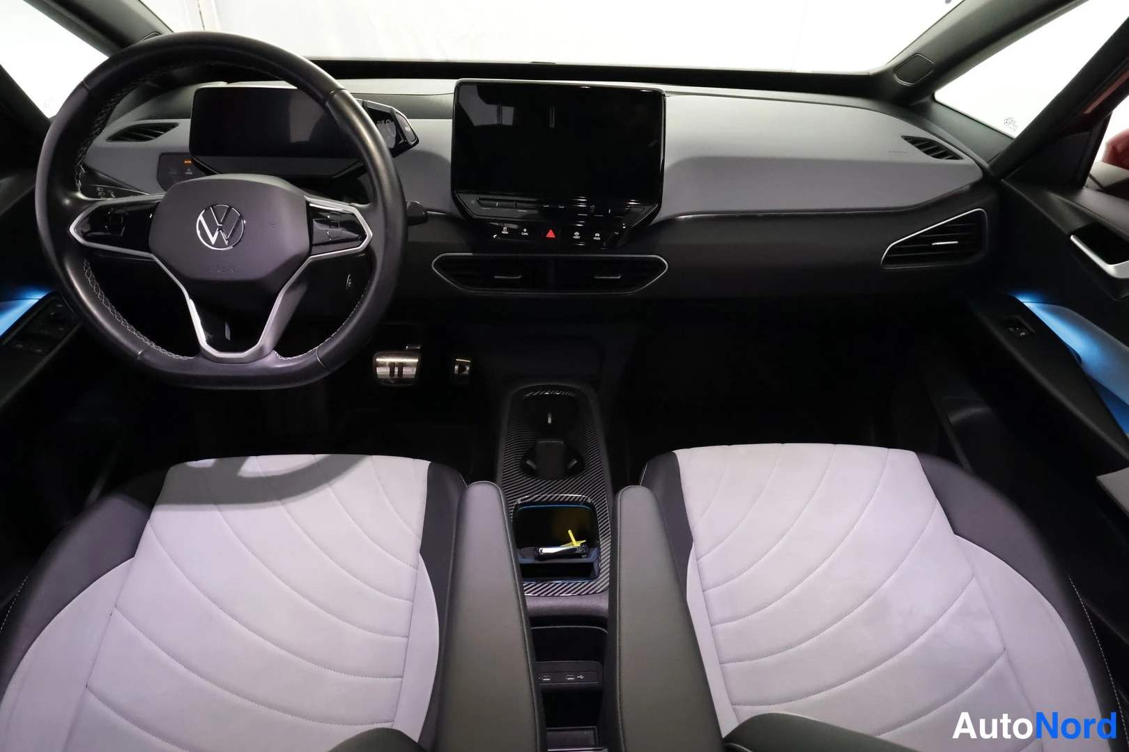 Etuistuimet: Interior view of the front cabin showing two front seats with grey fabric and dark inserts, a digital instrument cluster behind the steering wheel, a central in