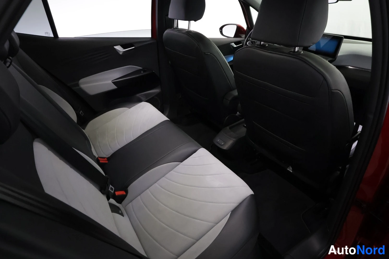 Takaistuimet: Rear seating area viewed from an open side door, showing bench seat with grey and dark upholstery similar to front seats, headrests, seatbelts, and carpeted flo
